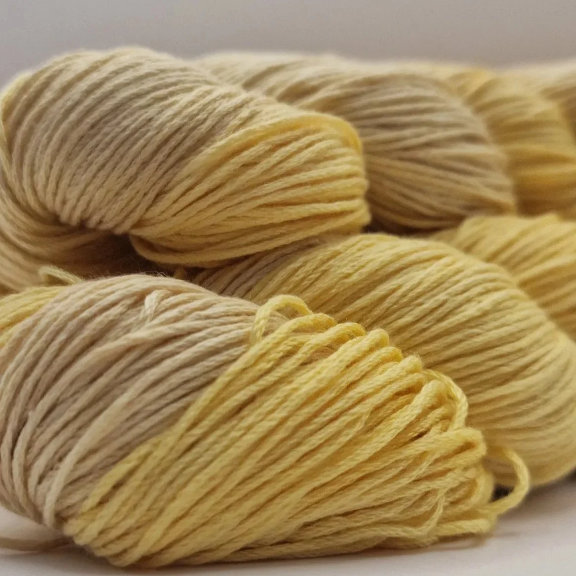 Handgefärbtes Lyocell Garn im Farbverlauf von einem weichen Sandbeige zu einem warmen Gelb auf hellem Untergrund