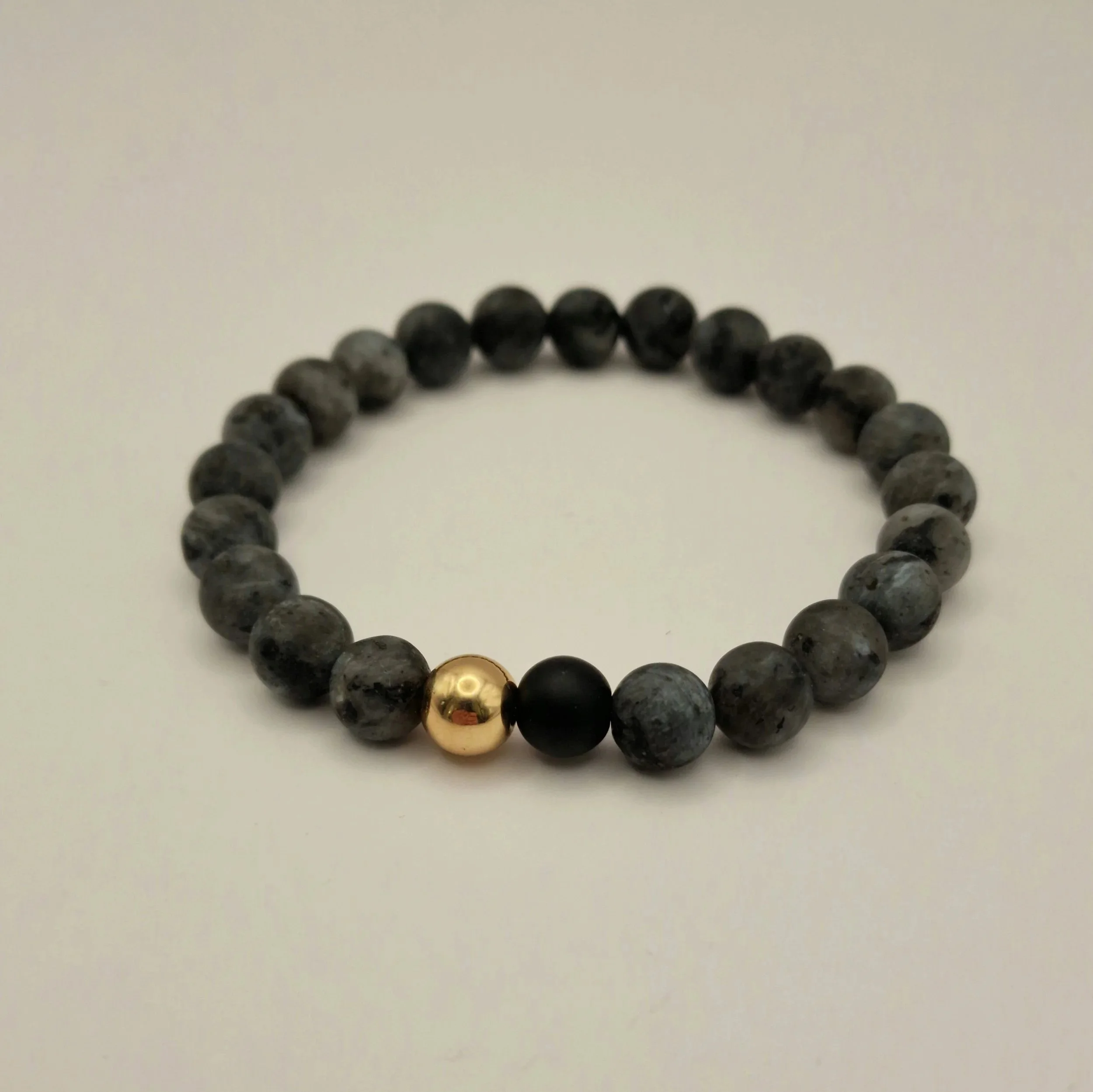Armband aus schwarzem mattem Labradorit und mattem Obsidian und vergoldetem Hämatit auf weißer Oberfläche liegend