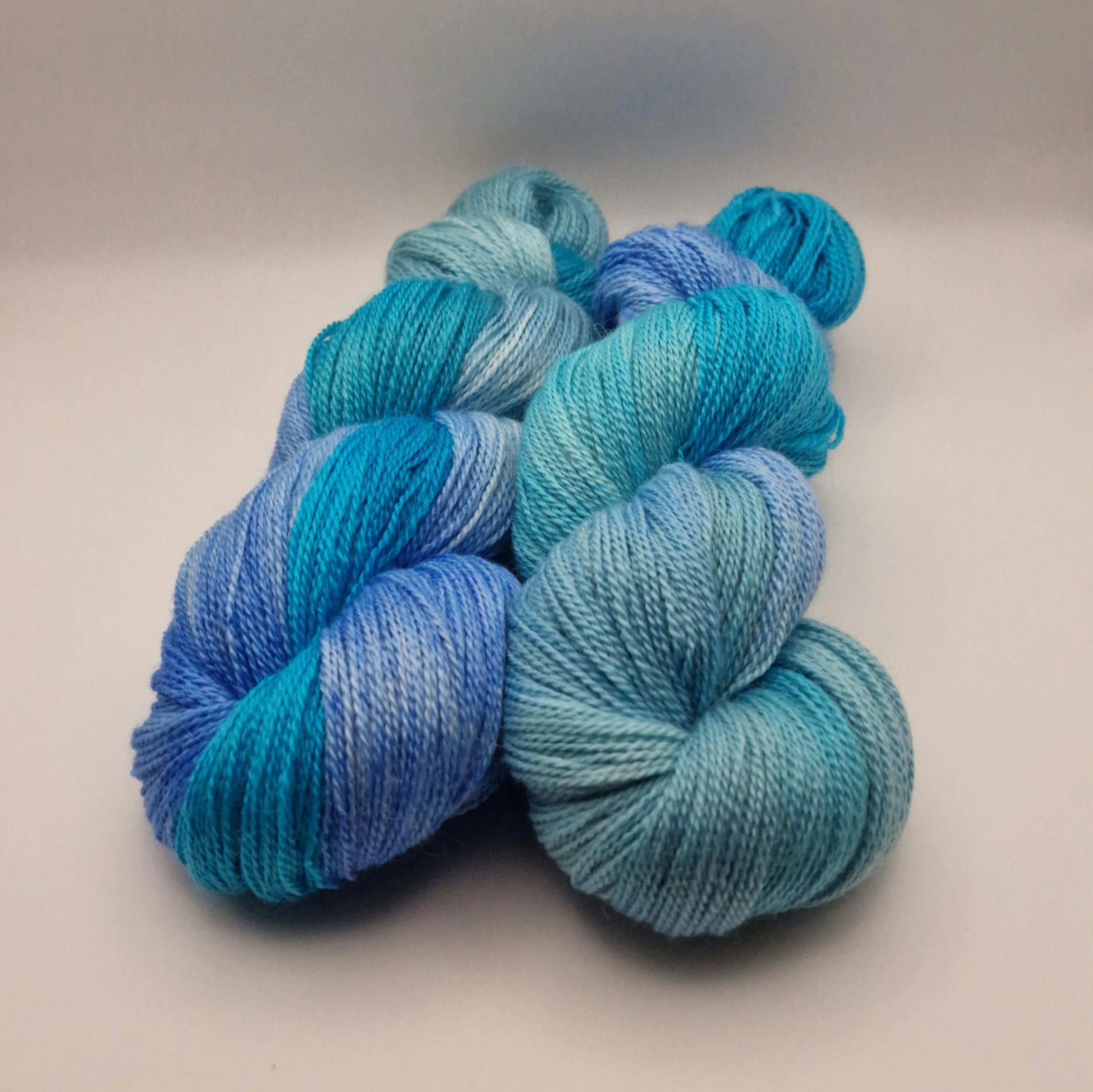 handgefärbte Stränge Wolle aus Schurwolle, Alpaka und Seide in blau, türkis und hellgrün auf weißem Untergrund das an Tropische Gewässer erinnert