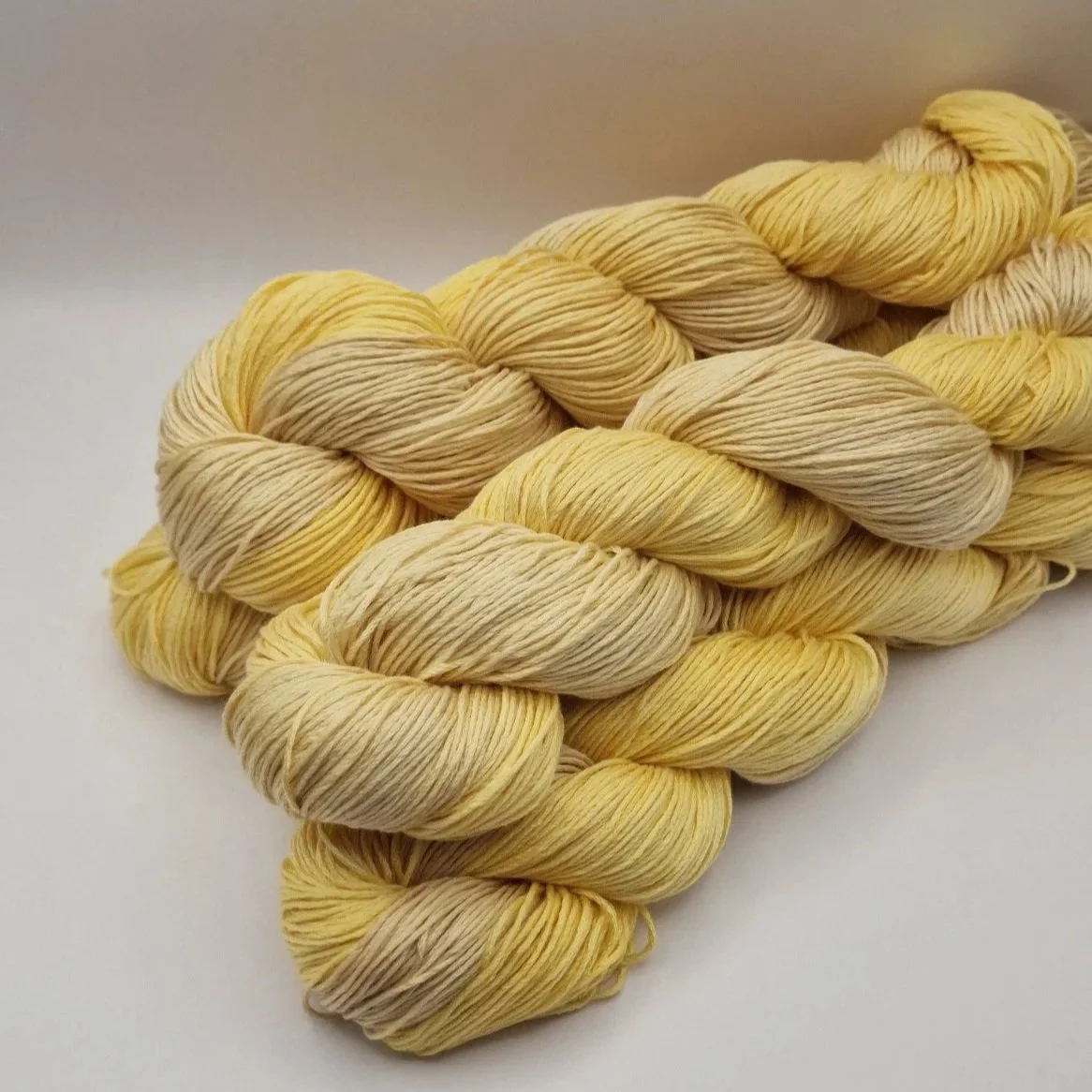 Handgefärbtes Lyocell Garn im Farbverlauf von einem weichen Sandbeige zu einem warmen Gelb auf hellem Untergrund