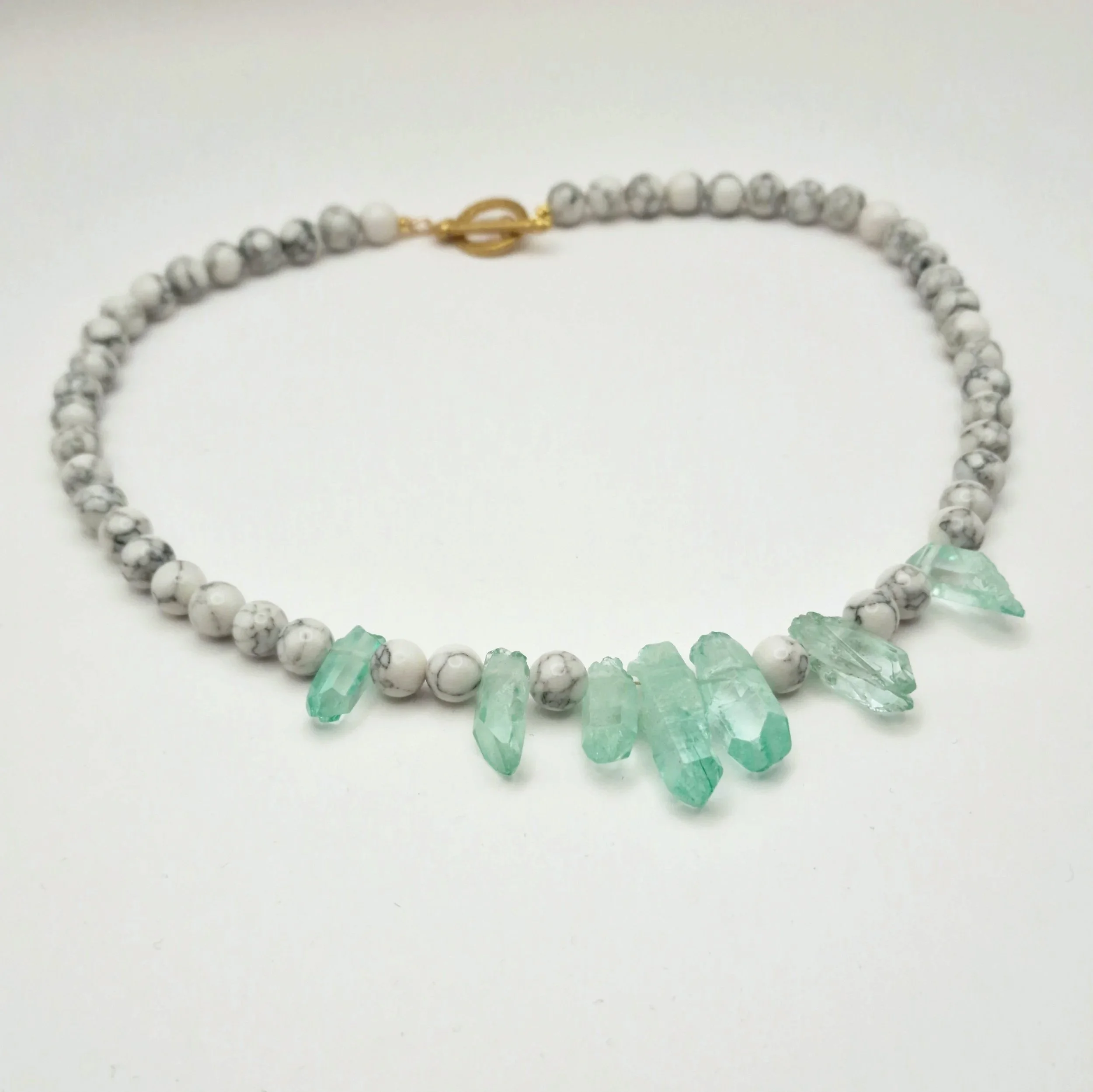 Kette aus weißen Howlith Perlen mit grün gefärbten Kristallspitzen und vergoldetem Verschluss  auf hellem Untergrund