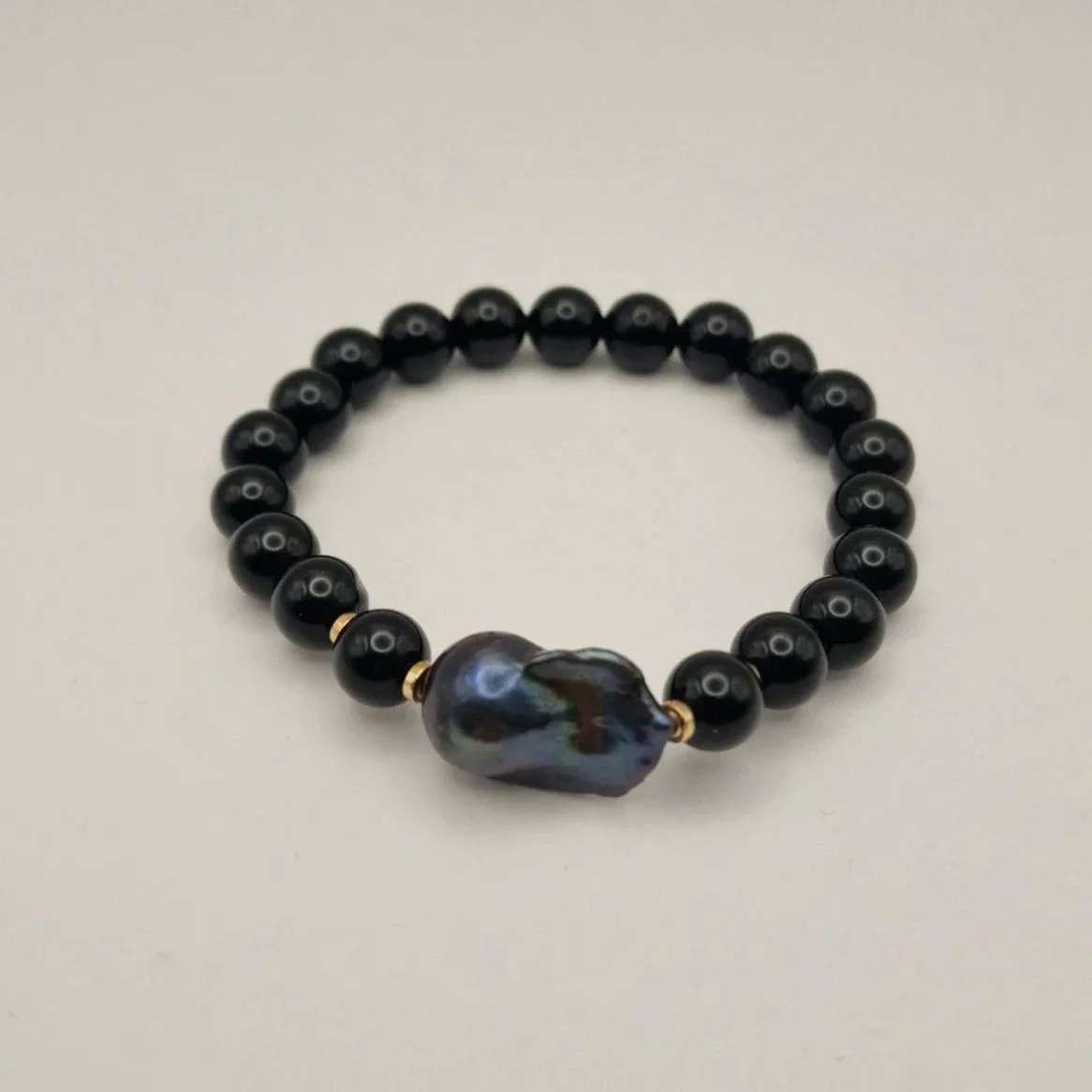 Armband aus Perlen von schwarzem Onyx, vergoldete Hämatitspacer und schwarzer Barockperle auf hellem Untergrund