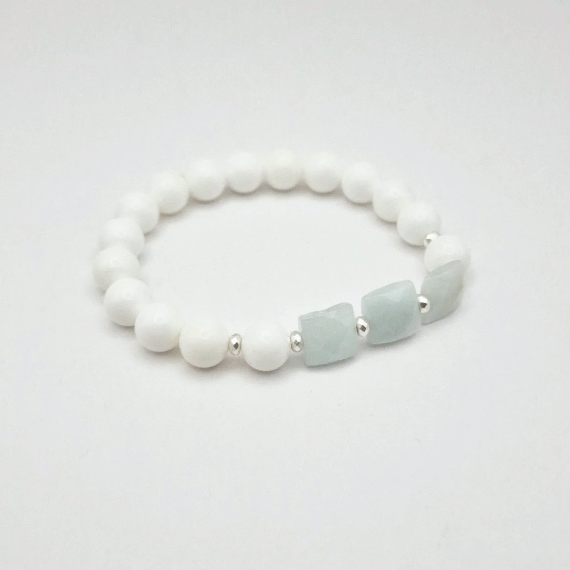 Armband aus weißen Koralleperlen mit versilberten Hämatit Spacern und eisblauen facettierten Rechtecken aus Aquamarin auf hellem Untergrund