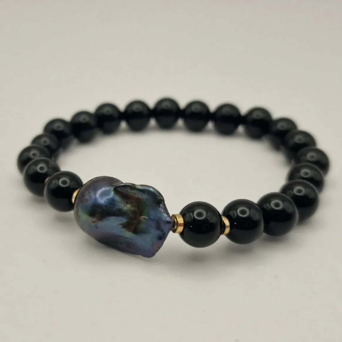 Armband aus Perlen von schwarzem Onyx, vergoldete Hämatitspacer und schwarzer Barockperle auf hellem Untergrund