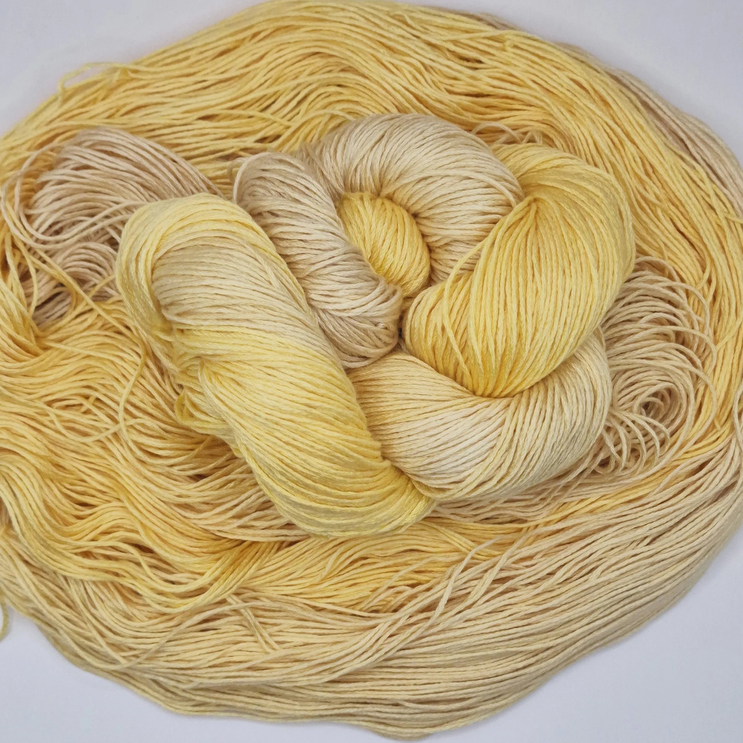 Handgefärbtes Lyocell Garn im Farbverlauf von einem weichen Sandbeige zu einem warmen Gelb auf hellem Untergrund