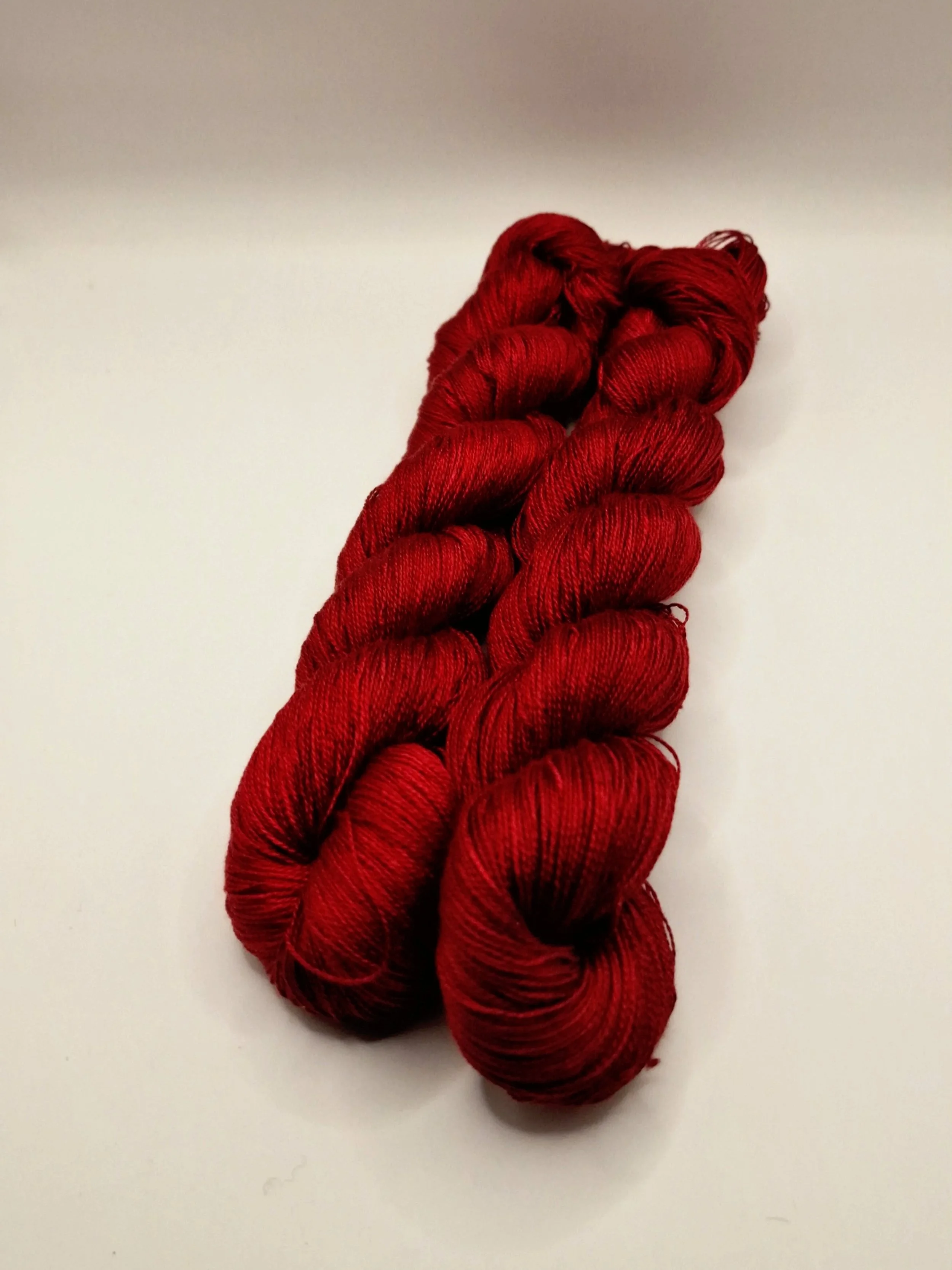 handgefärbte blutrote Seide in 2 Strängen auf hellem Untergrund