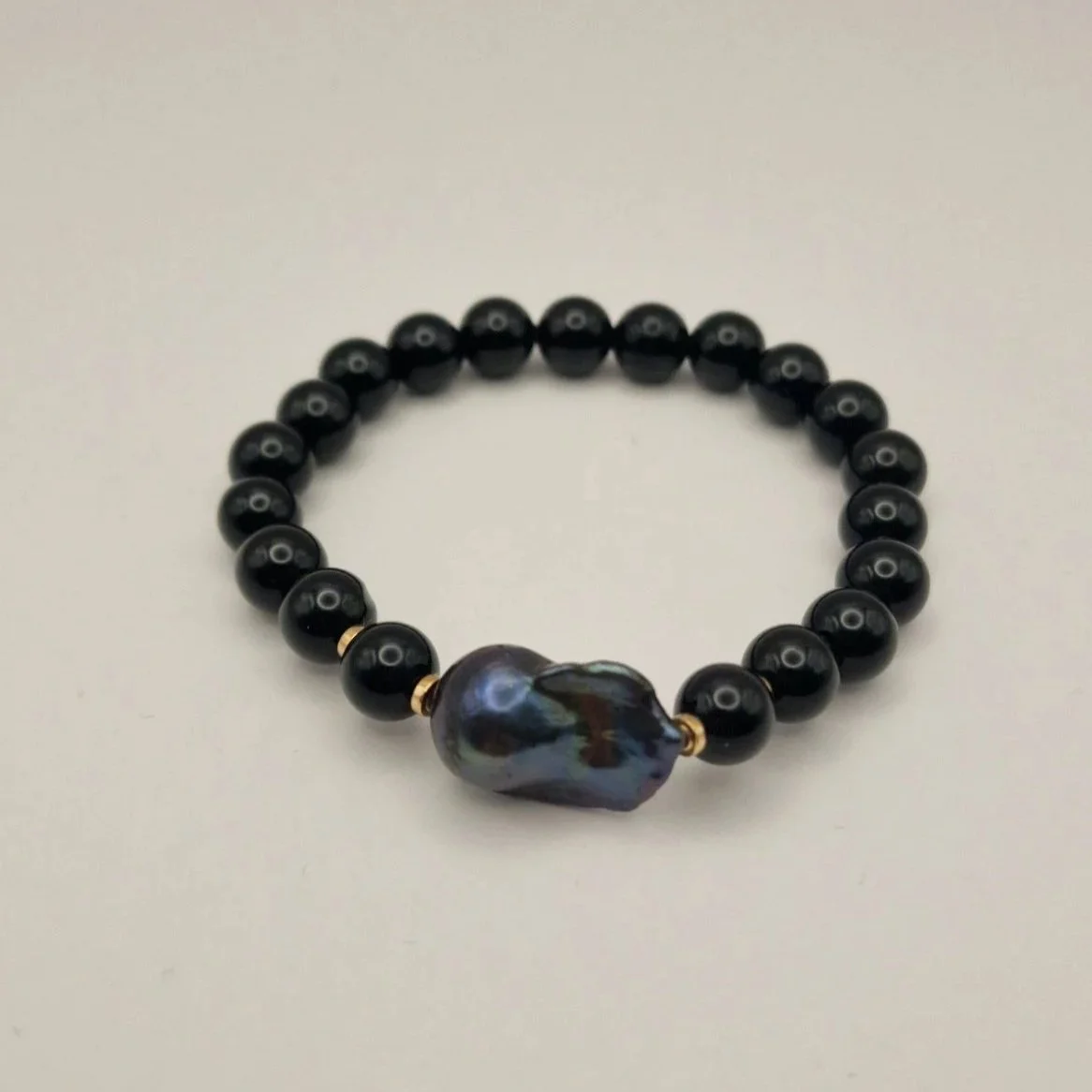 Armband aus Perlen von schwarzem Onyx, vergoldete Hämatitspacer und schwarzer Barockperle auf hellem Untergrund