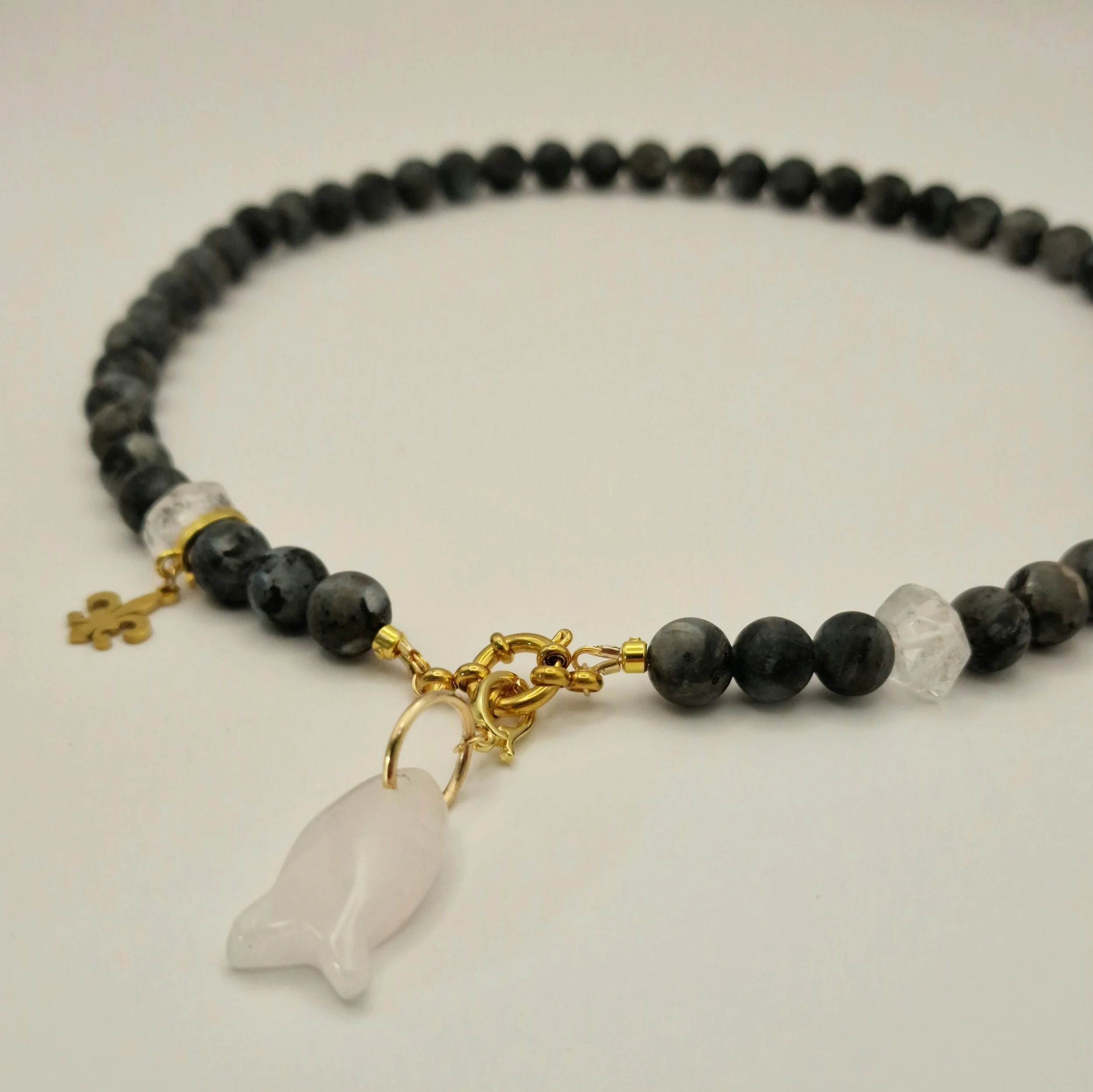 Kette aus schwarzen Spektroliit Perlen kombiniert mit Bergkristall und einem Fischanhänger aus feinem Rosenquarz auf hellem Untergrund