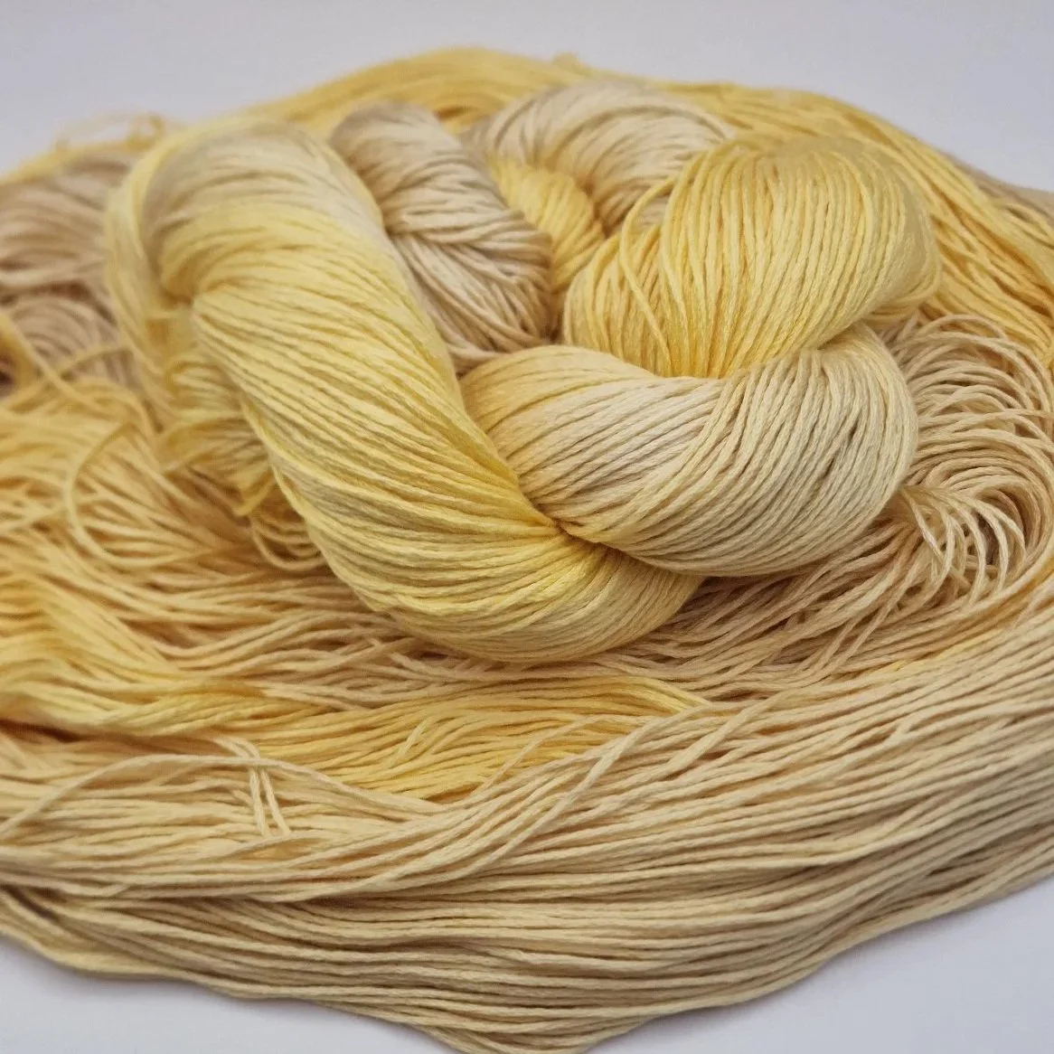 Handgefärbtes Lyocell Garn im Farbverlauf von einem weichen Sandbeige zu einem warmen Gelb auf hellem Untergrund