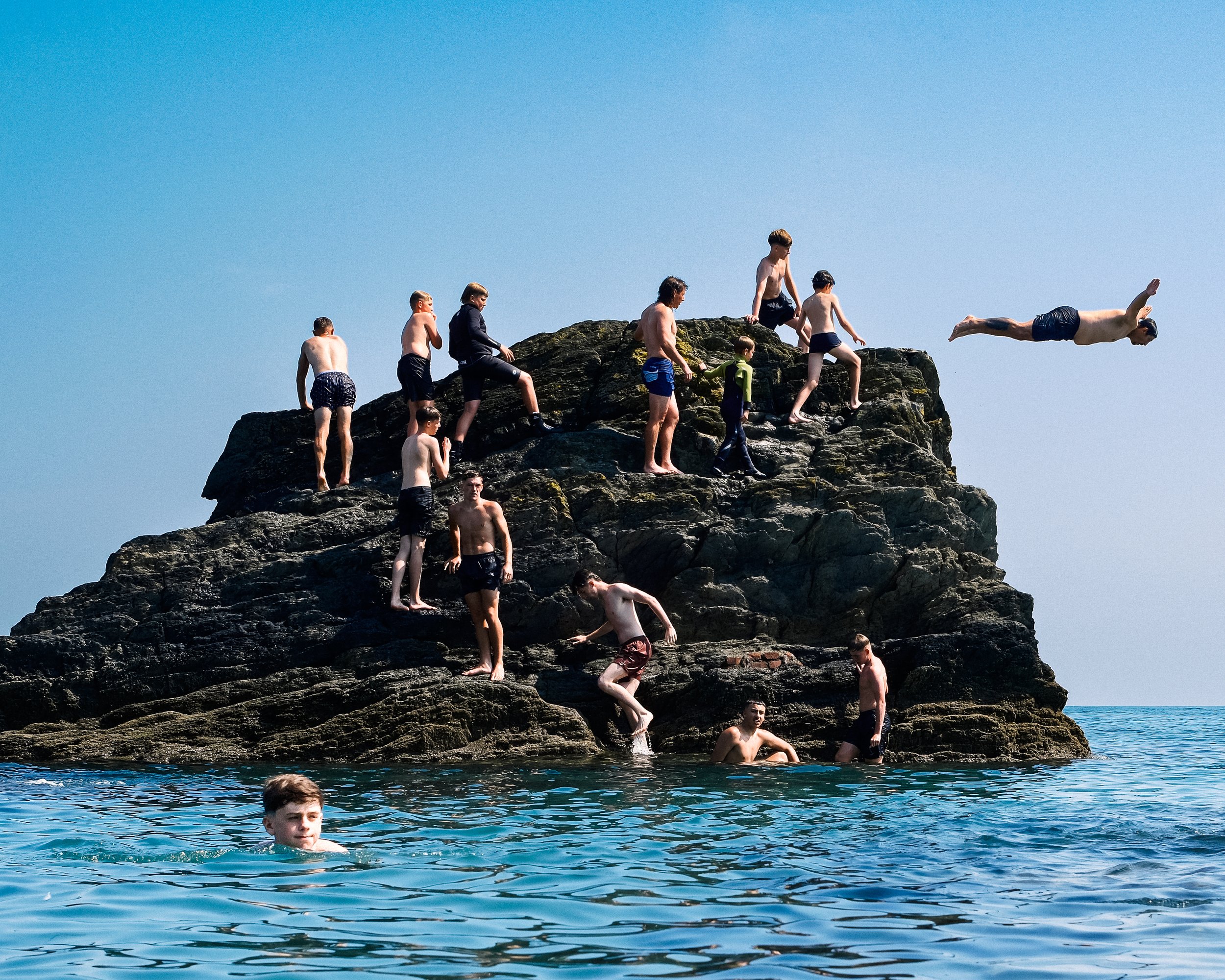 Group of people jumping off a rocky cliff into the water during daytime.
