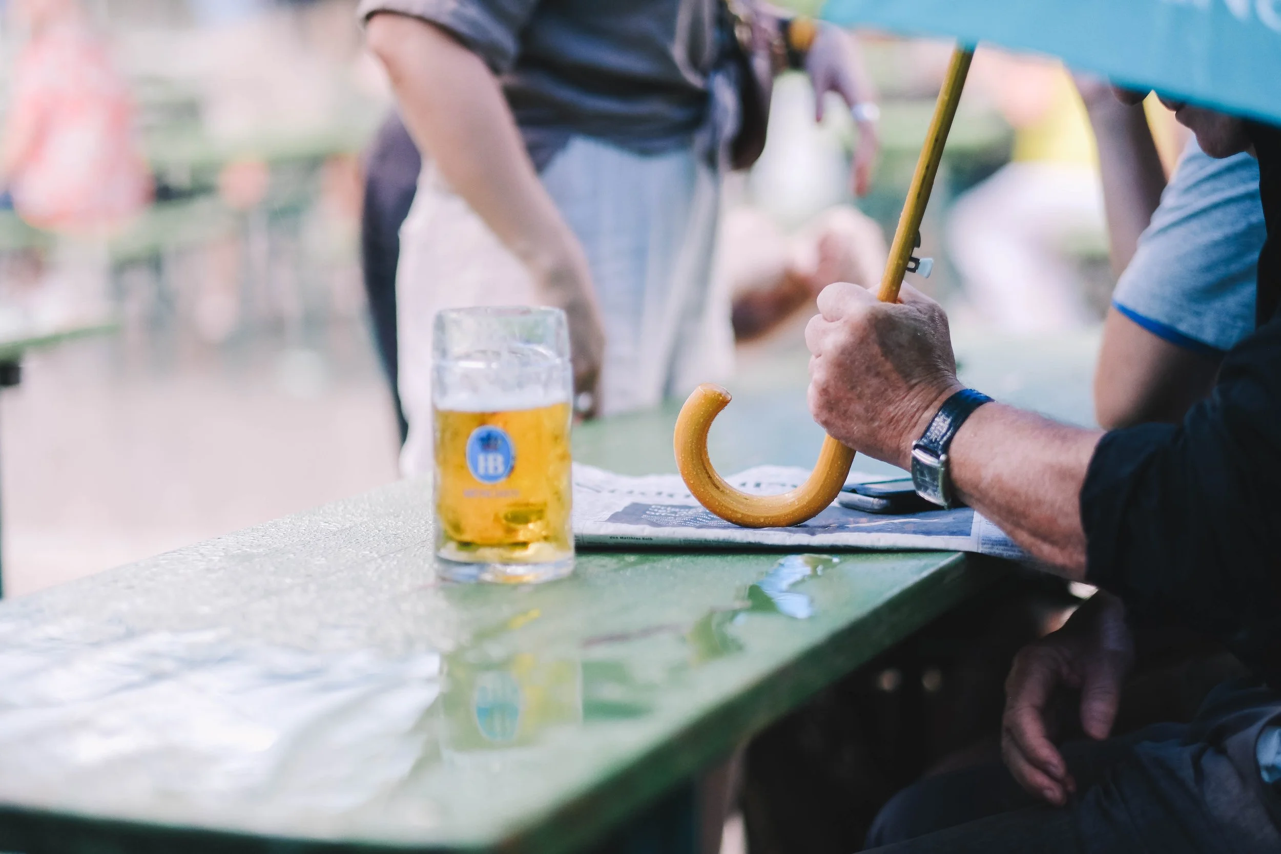 A person holding an umbrella handle next to a glass of beer on a green table.