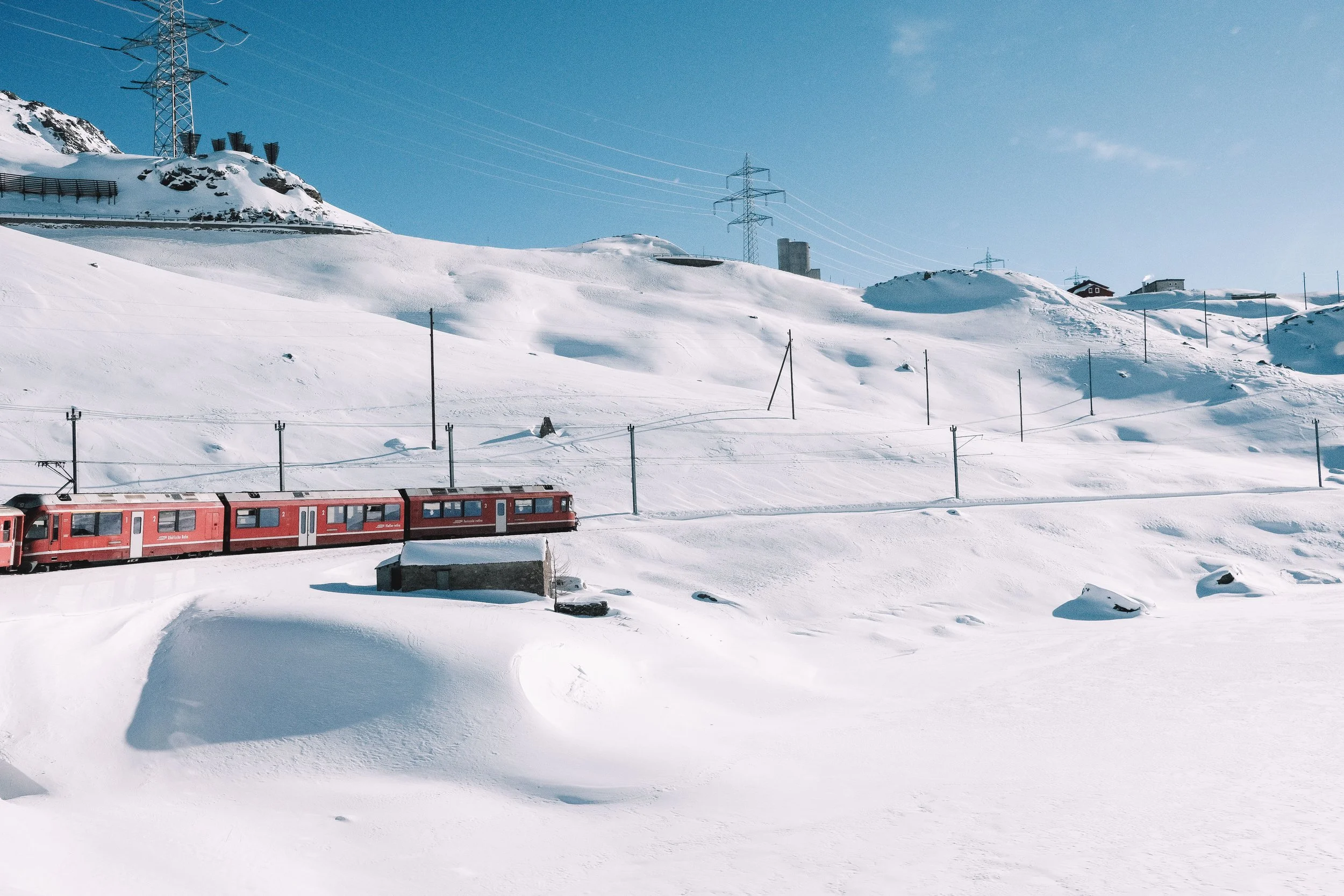 Red train traveling through snowy landscape with blue sky