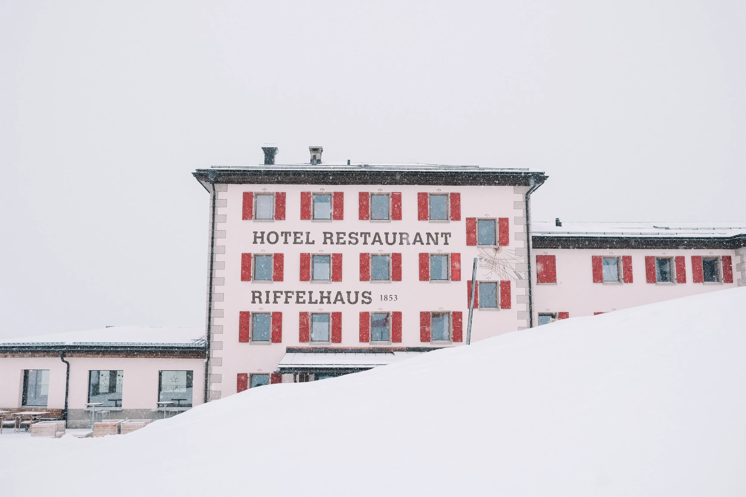 Hotel Riffelhaus building covered in snow with red window shutters and cloudy sky.