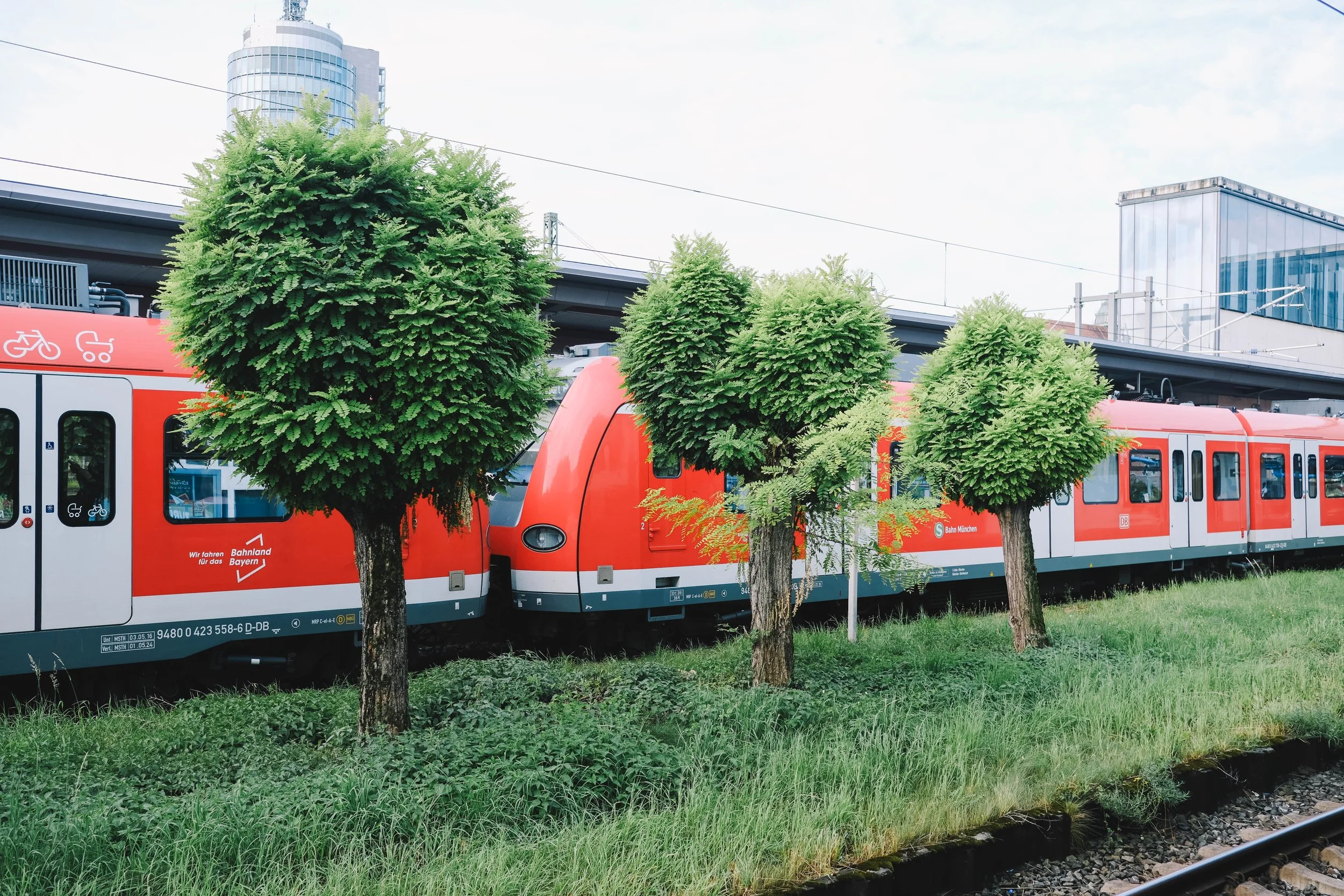 Red train at a station with trees in the foreground.