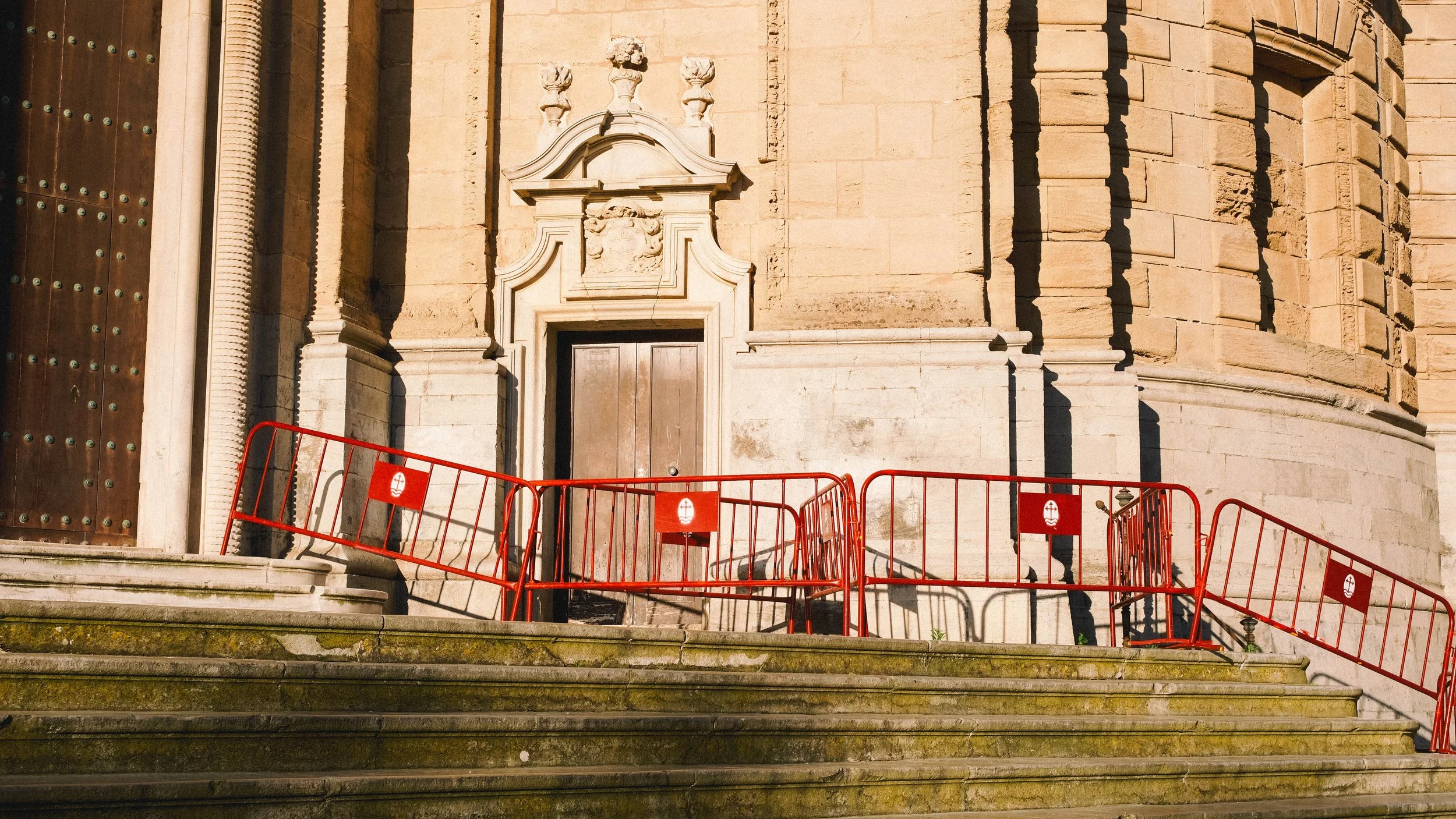 Stone steps leading up to an ornate building entrance, with red construction barriers in front.