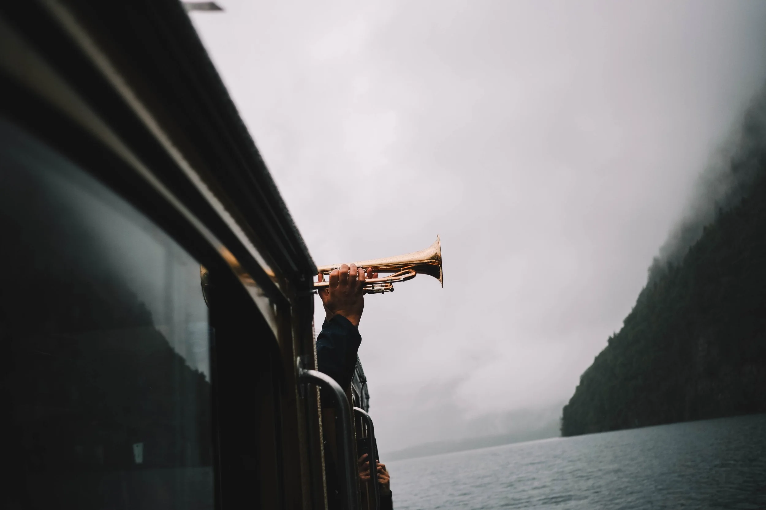 Person holding trumpet out of a bus window over a misty lake
