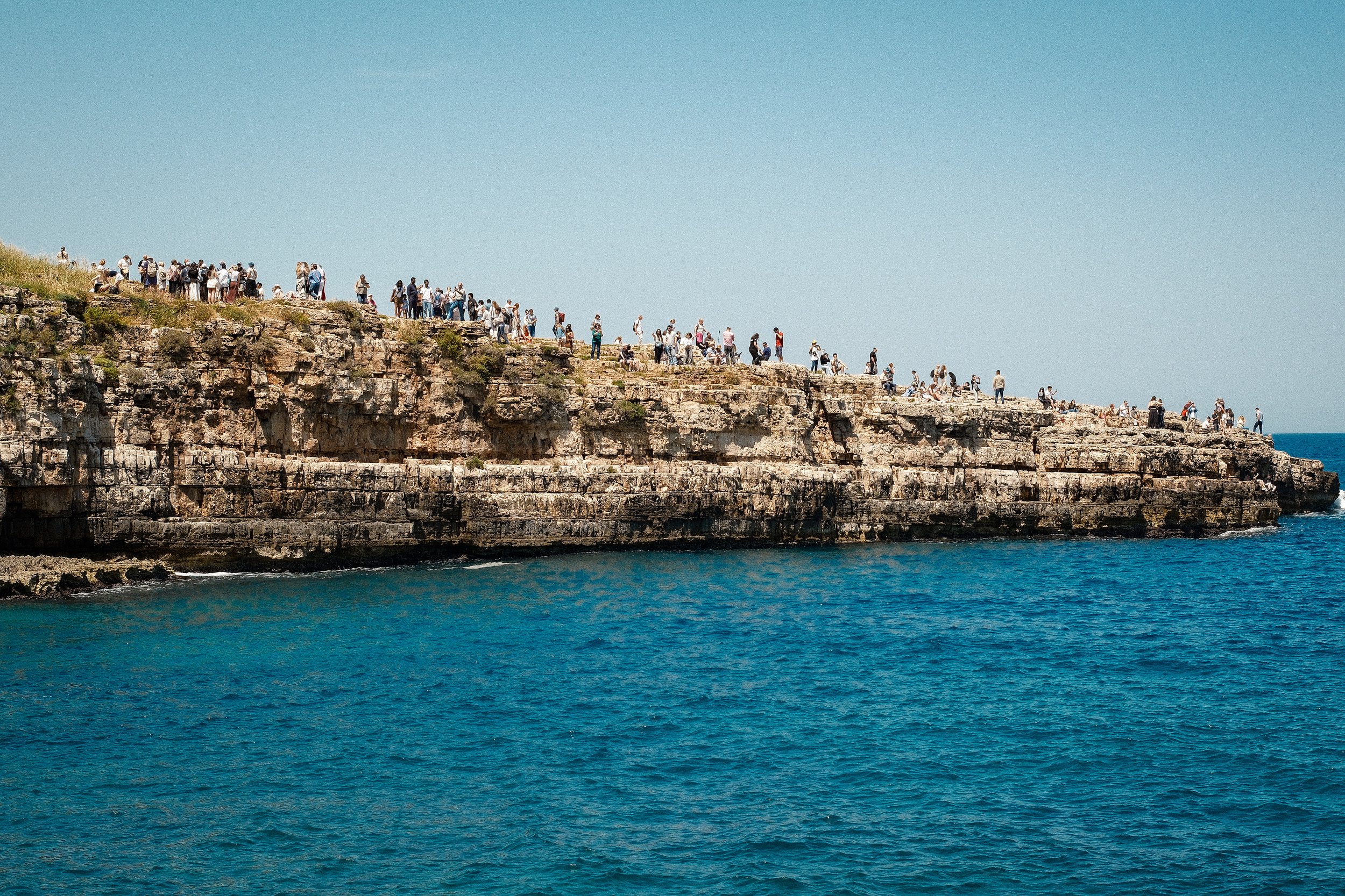Cliff with many tourists overlooking the ocean on a clear day.