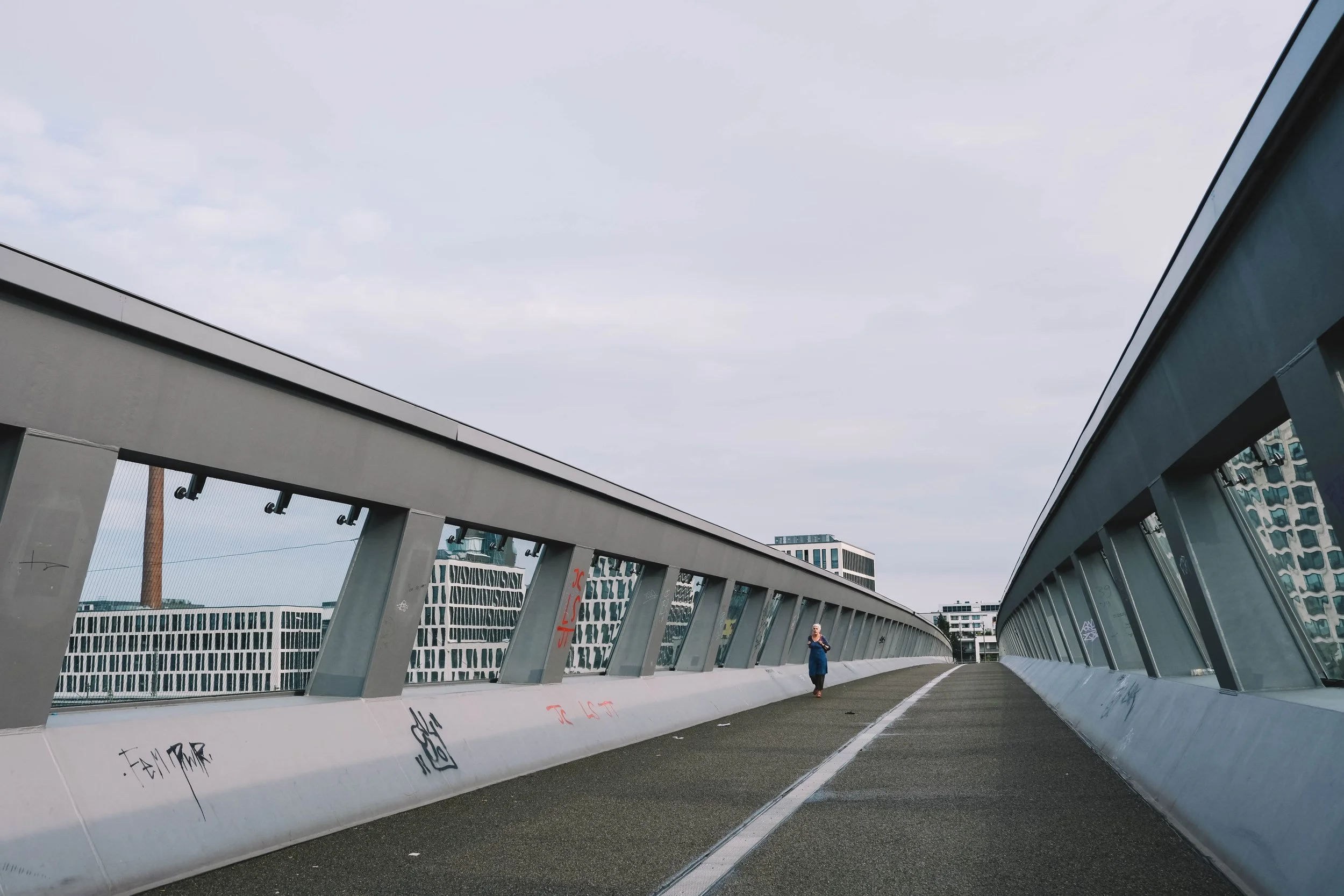 Urban pedestrian bridge with person walking, surrounded by modern buildings.