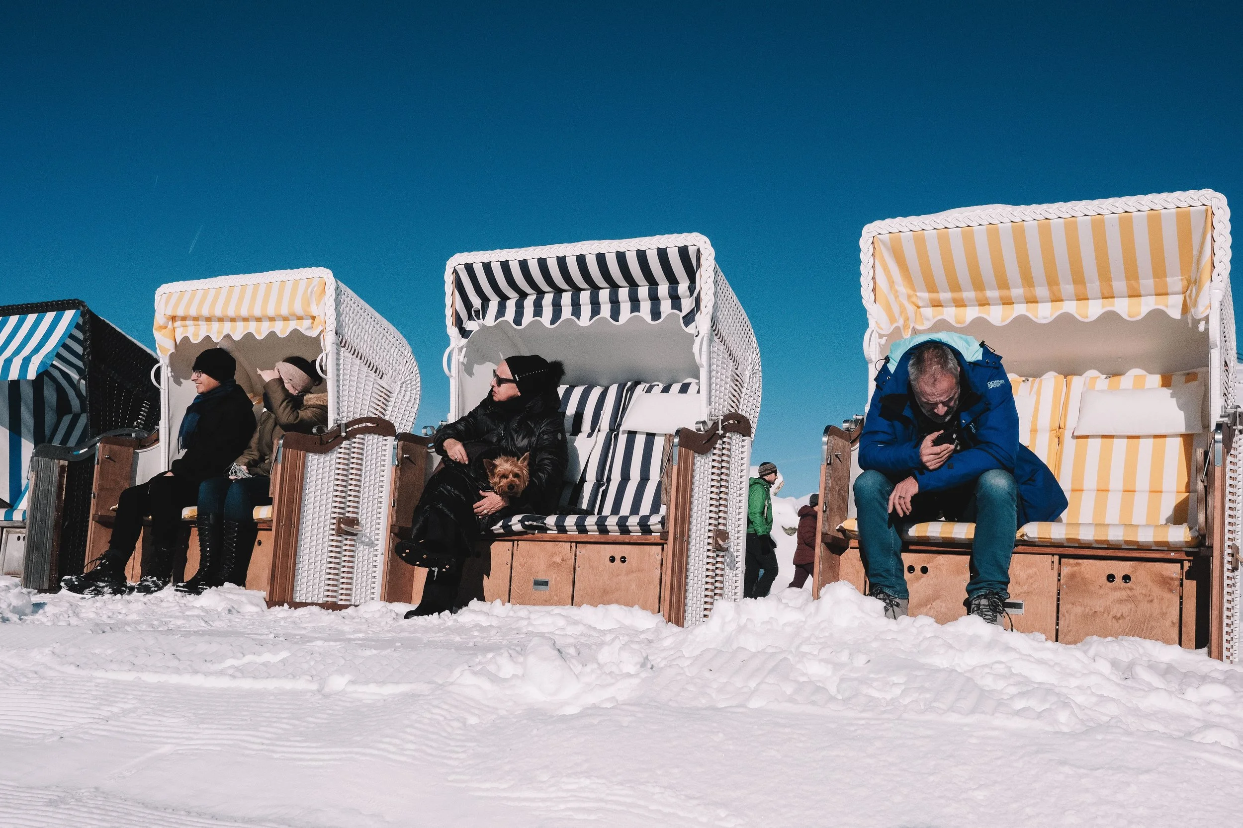 People sitting in wicker beach chairs with striped covers on a snowy landscape.
