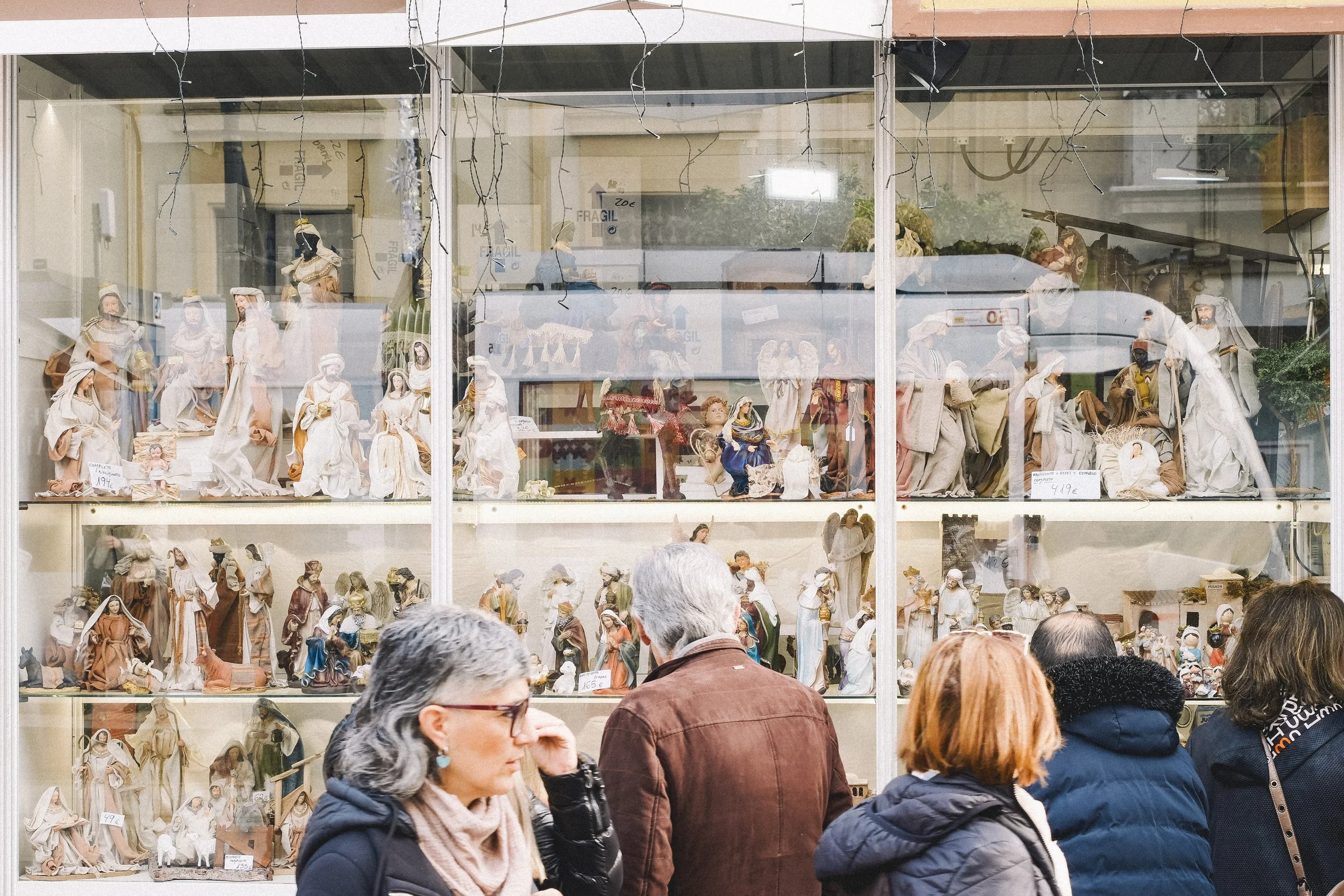 Shop window displaying nativity figurines with people looking at them outside.
