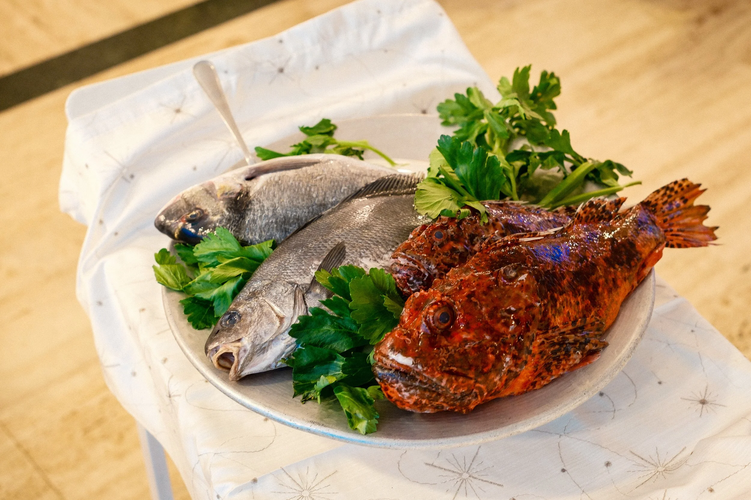 Fresh fish on a white plate garnished with green herbs, set on a table.
