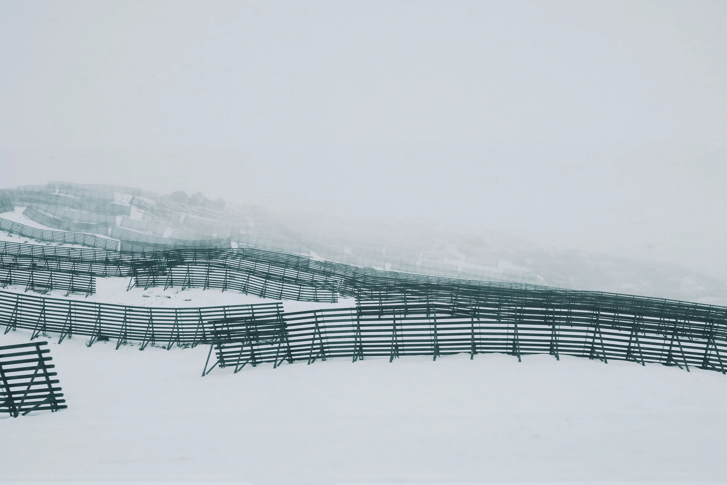 Snow-covered landscape with wooden snow fences in foggy conditions.