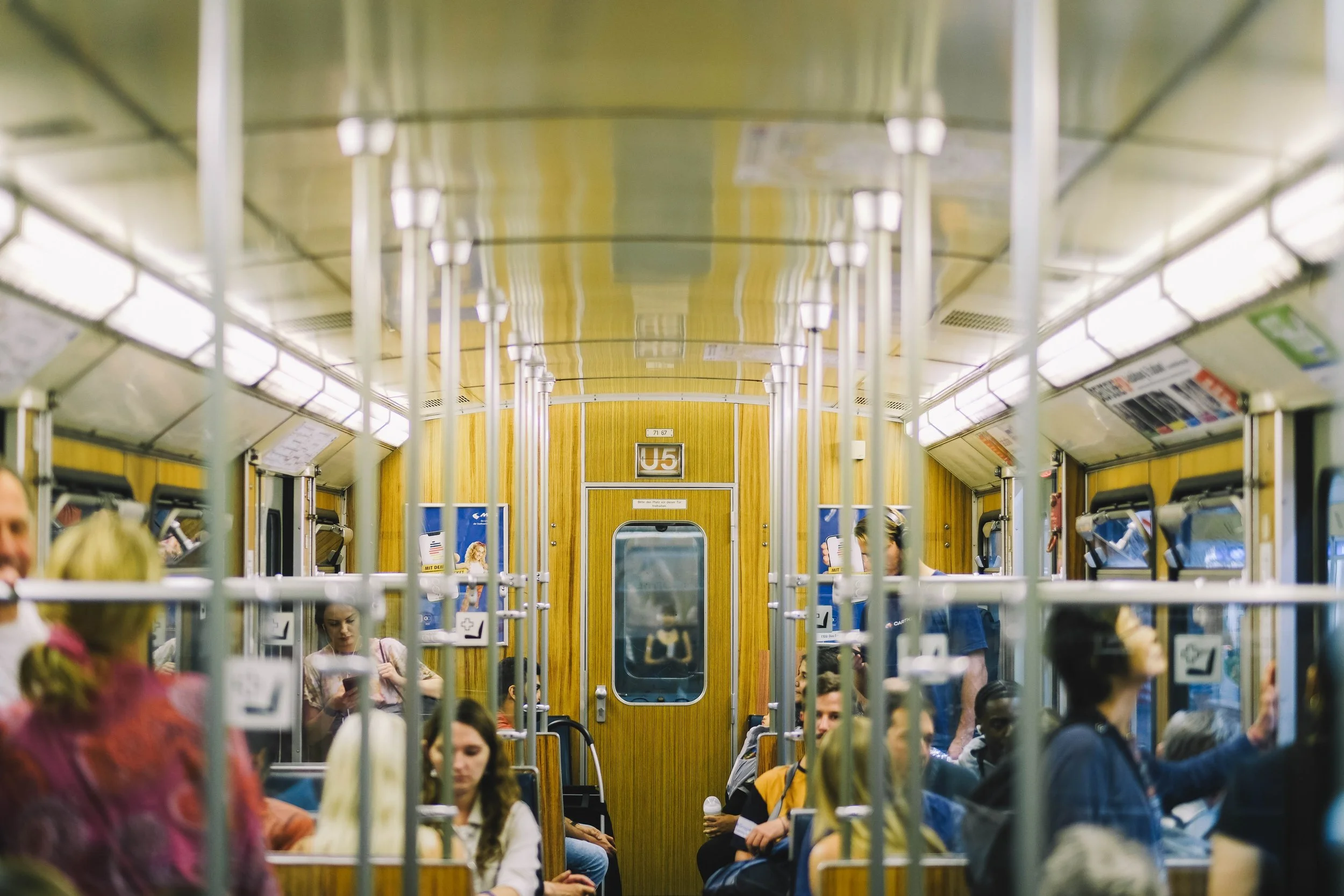 Interior of a subway train car with seated and standing passengers, wood-paneled walls, metal poles, and a "U5" sign above the door.
