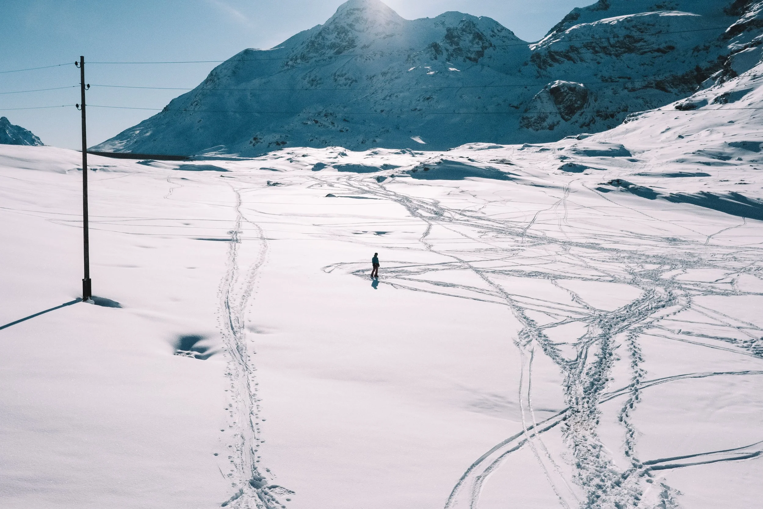 Person skiing on a snow-covered landscape with mountains in the background and ski tracks in the snow.