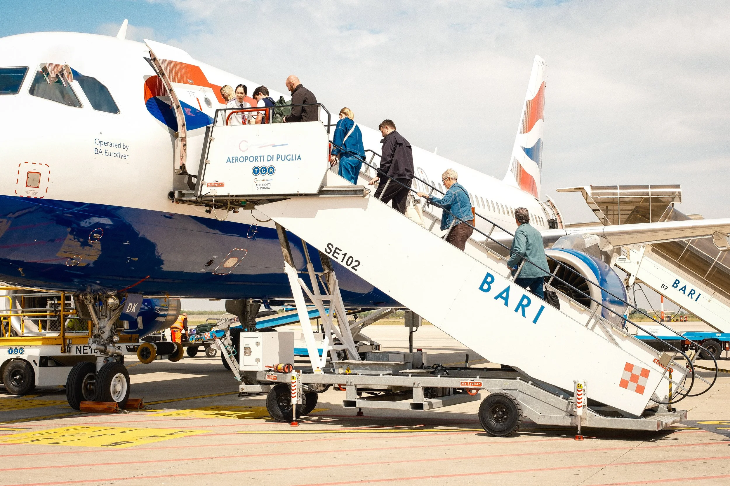Passengers boarding a commercial airplane via a mobile stairway at an airport tarmac on a partly cloudy day.