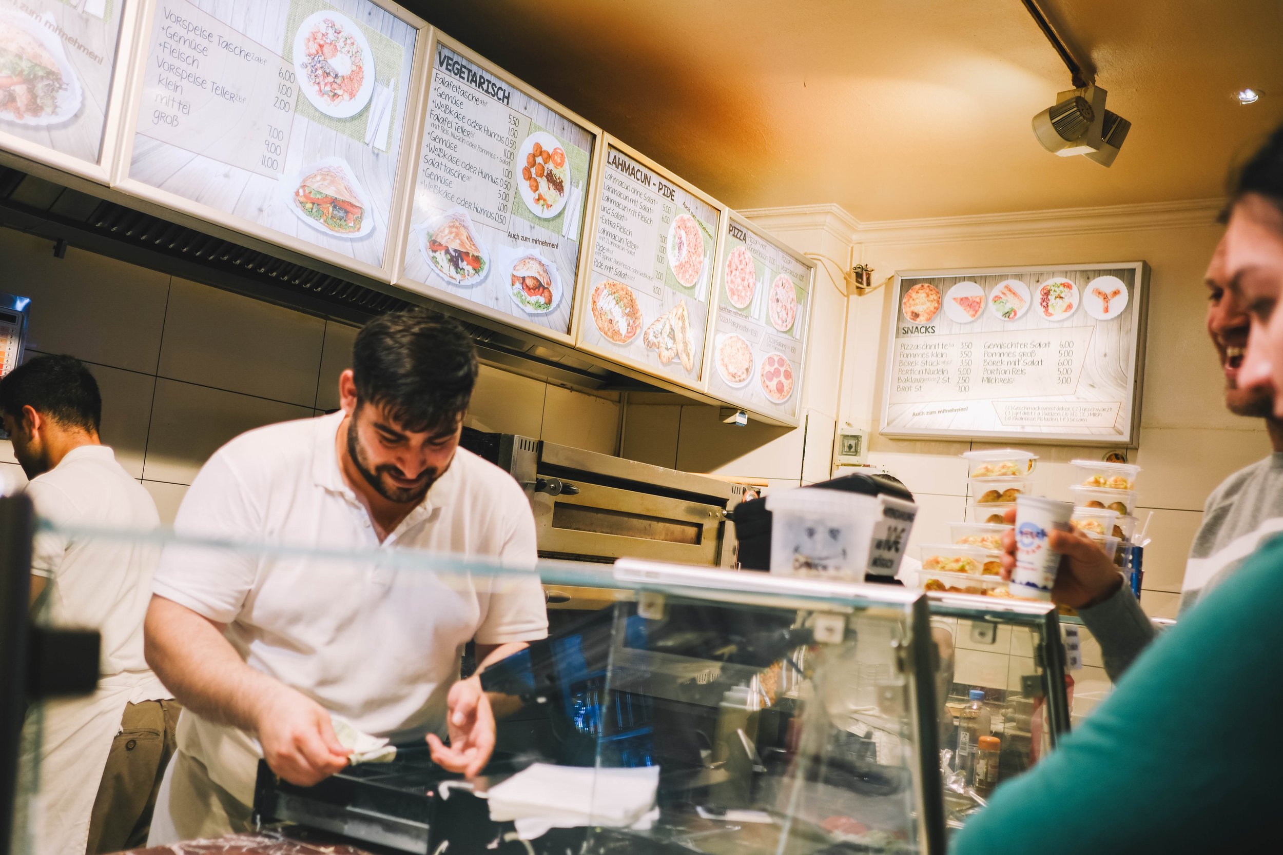 A man serving customers in a fast food restaurant with a menu on the wall.