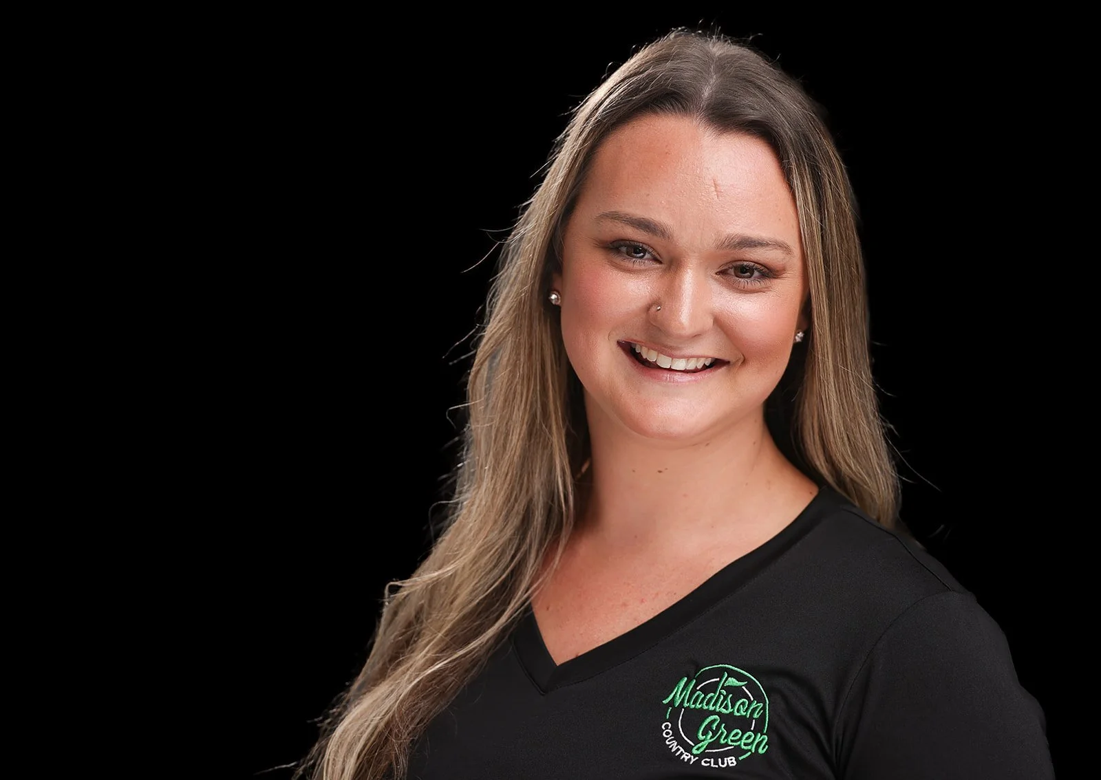 A smiling young woman with long, wavy hair wearing a black V-neck shirt with green embroidered logo that says 'Madison Green Country Club'.