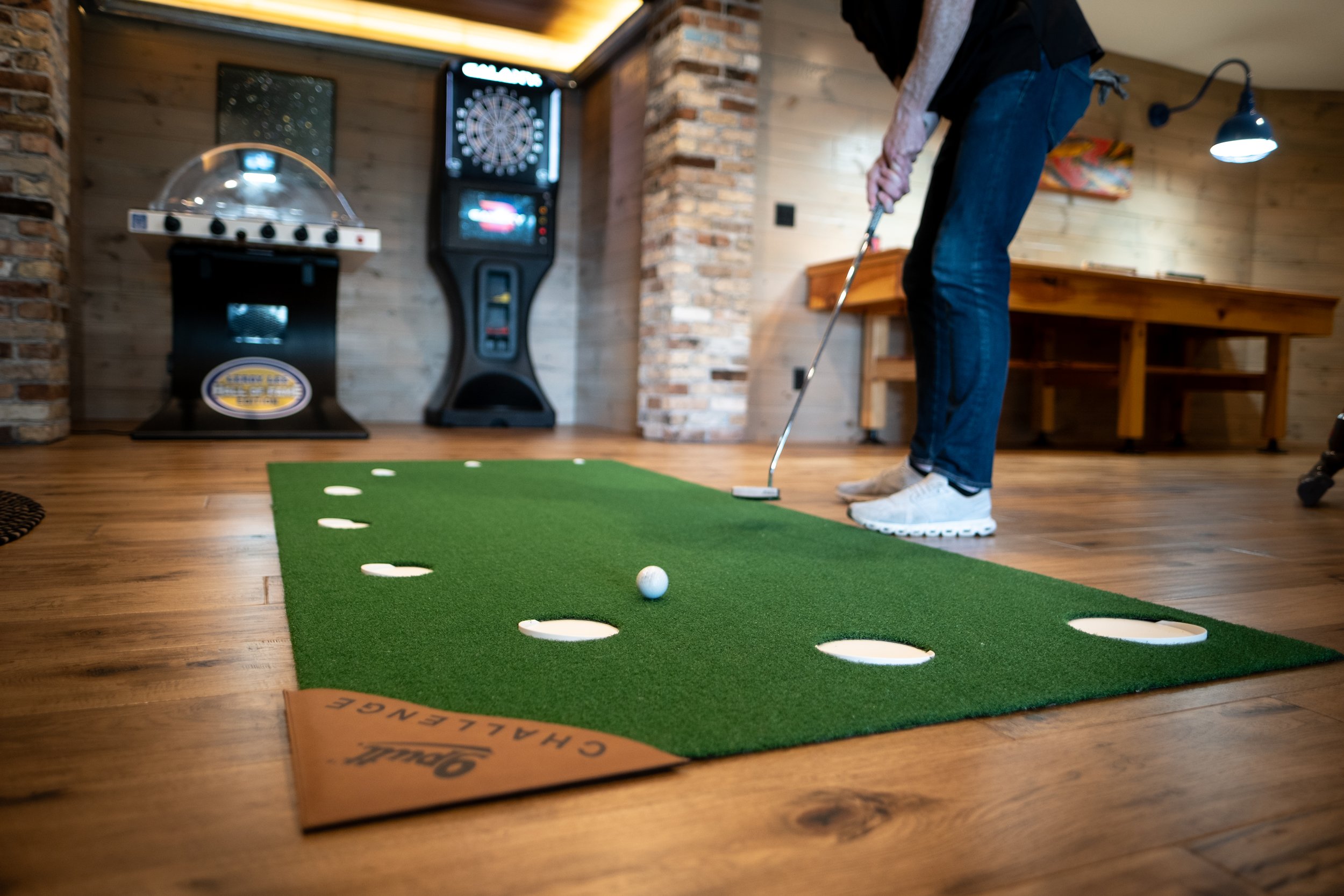 Person practicing mini golf indoors on a green putting mat with golf holes and a golf ball.