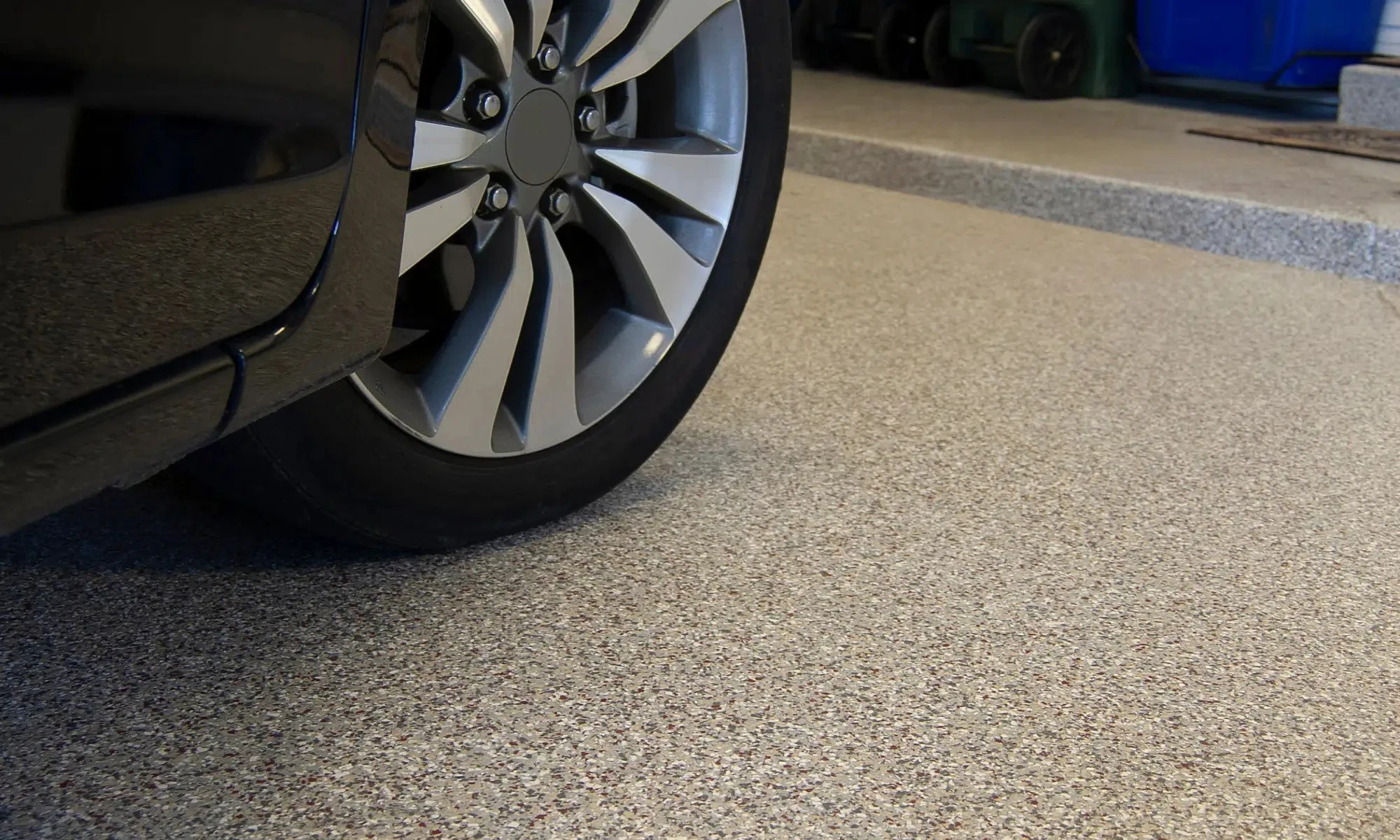 Close-up of a car wheel with a silver rim parked on a speckled concrete surface in a garage.