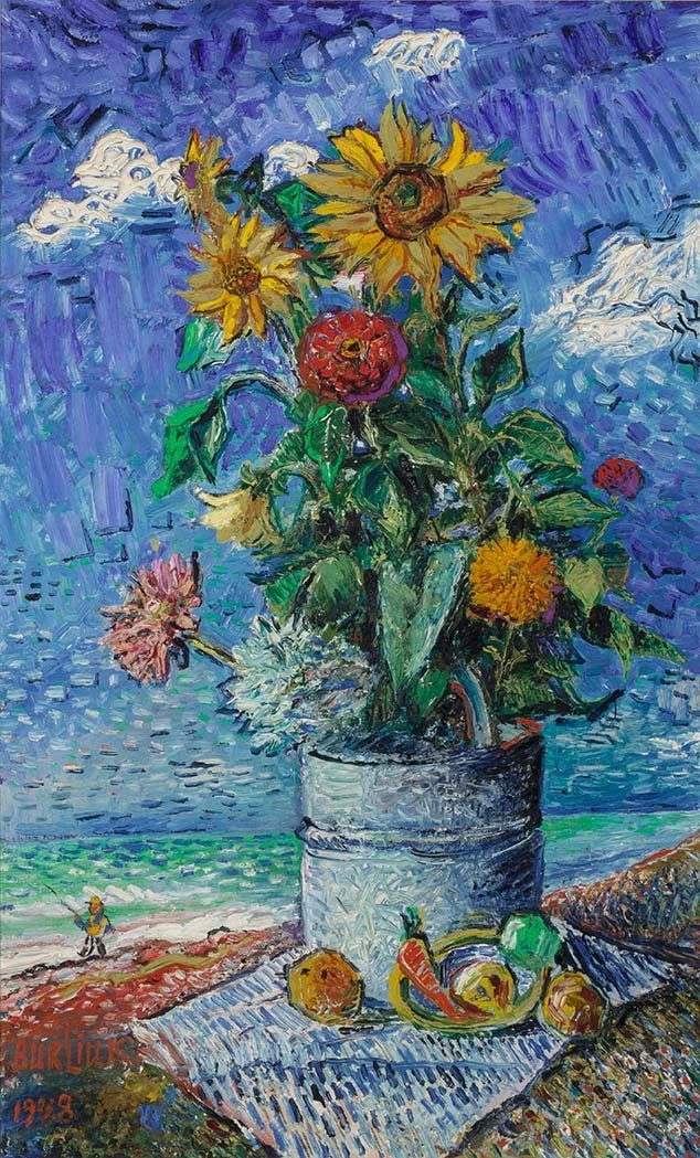 Vibrant bouquet of sunflowers and other blooms in a metal pail on a cloth-covered table, with fruit beside it and a fisherman fishing in the distance along a turquoise shoreline under a bright blue sky.