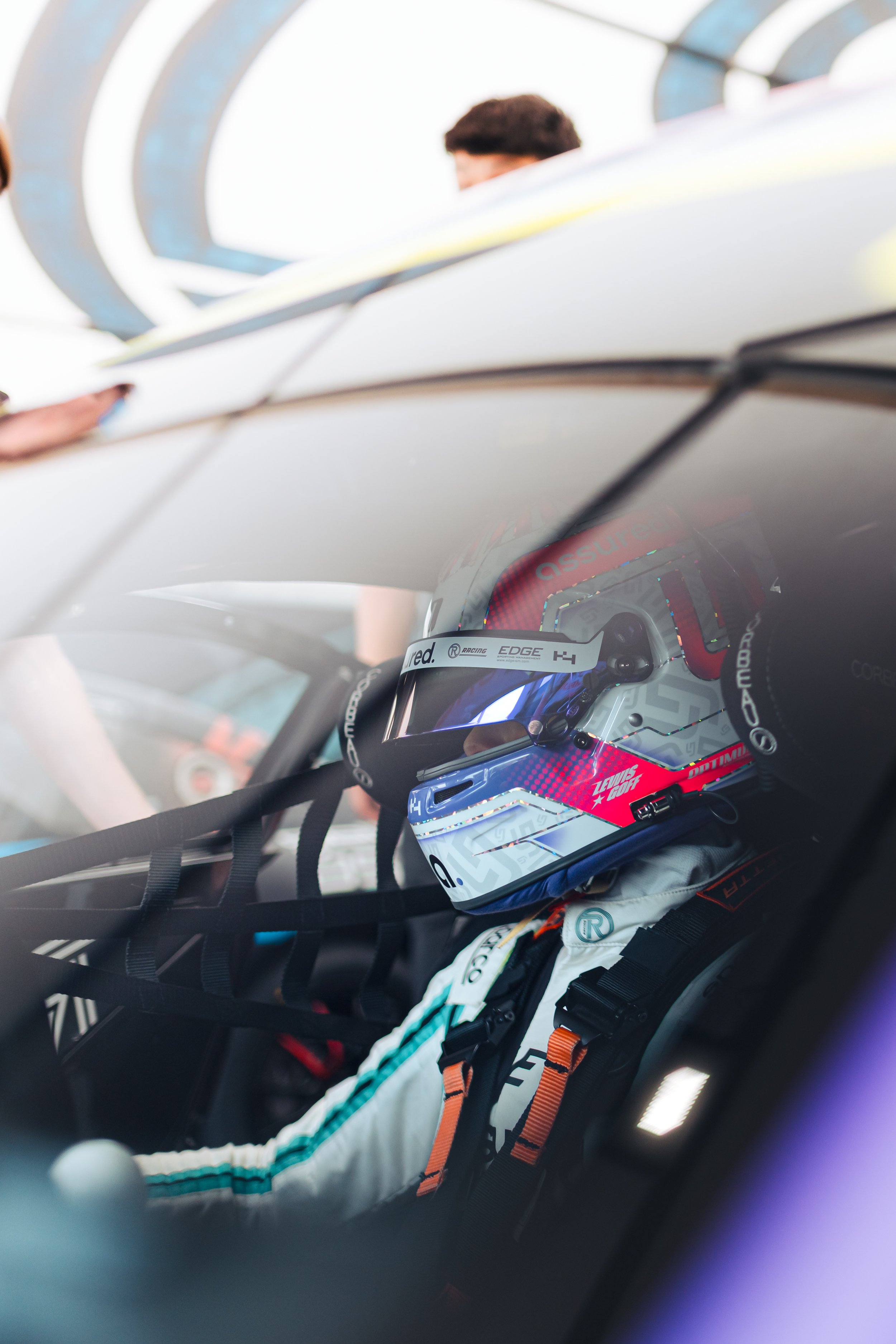 Lewis Goff, sitting in his Ginetta Junior Car, ready to go out and compete at Oulton Park circuit in the UK. He is wearing a white helmet, with Pink and Purple details.