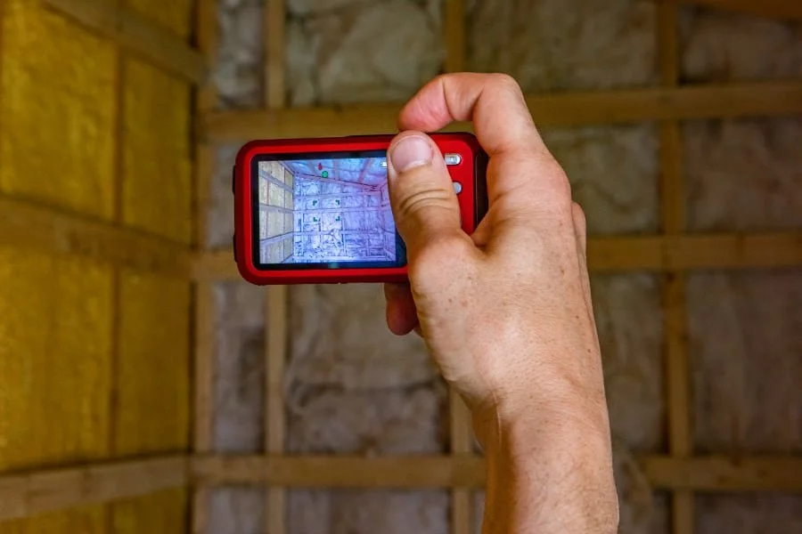 Home inspector using a thermal imaging camera to check exposed wall framing, insulation, and possible hidden issues during a residential inspection.