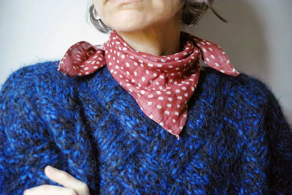 Close-up of a woman wearing a red polka dot bandana, a blue fuzzy sweater, and a portion of her face visible.