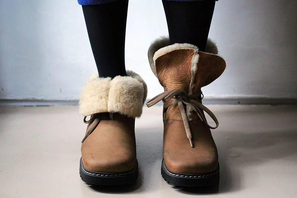 Pair of winter boots with faux fur lining worn over black leggings on a concrete floor.