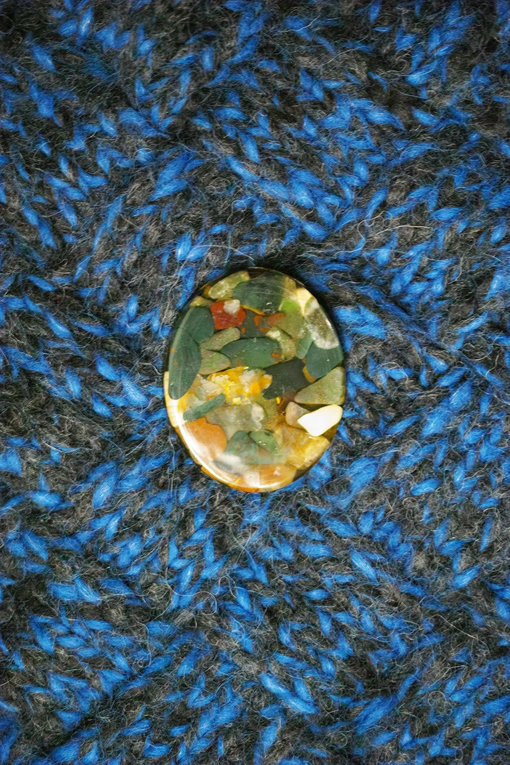 A close-up of a gemstone with a camo pattern, set on a black and blue knitted fabric.