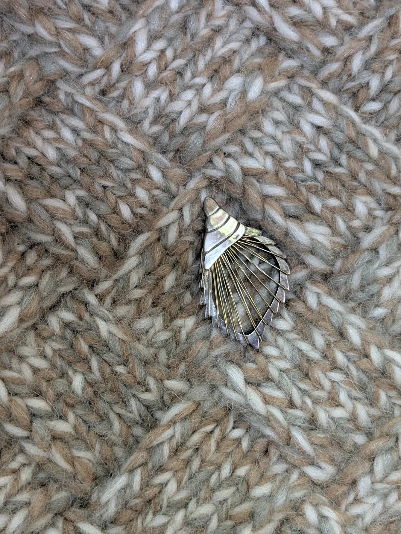 A decorative seashell brooch with a silver and gold design on a chunky beige knitted wool sweater.