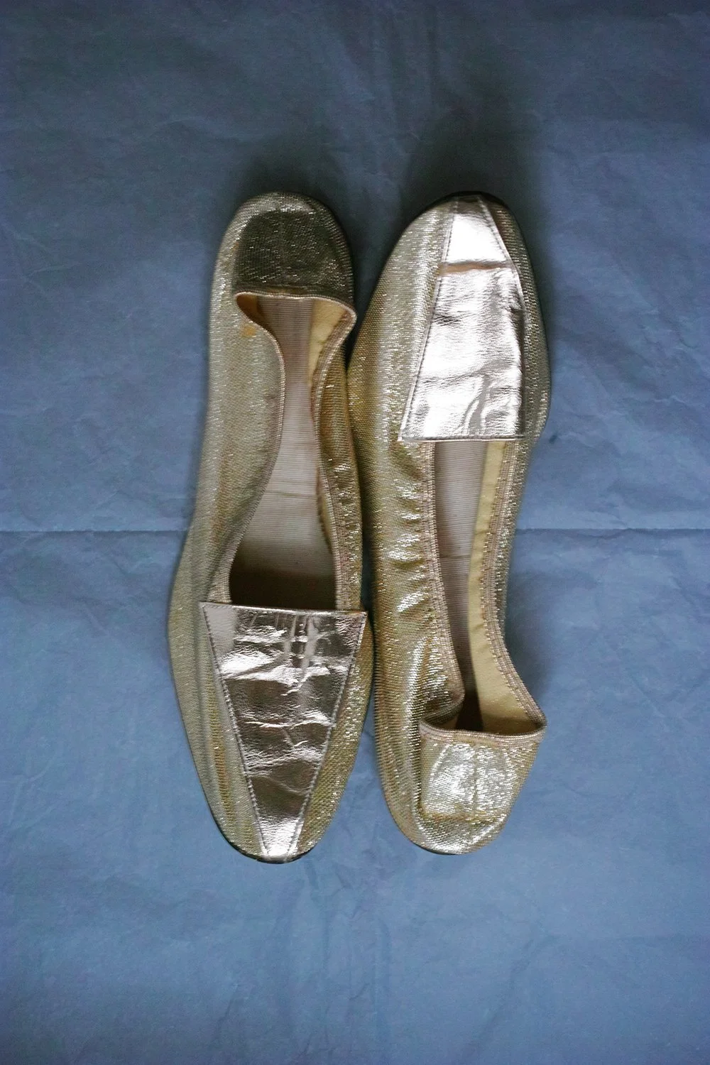 A pair of gold glittery ballet flats shoes with metallic accents on a blue surface.
