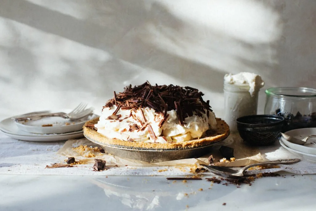 side shot of banana cream pie piled with whipped cream and chocolate shavings on top