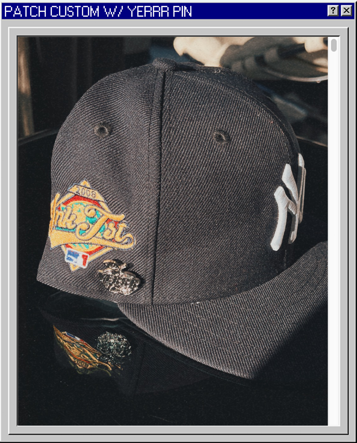 A black baseball cap with a colorful embroidered patch on the front and a white embroidered letter on the side, placed on a reflective black surface.