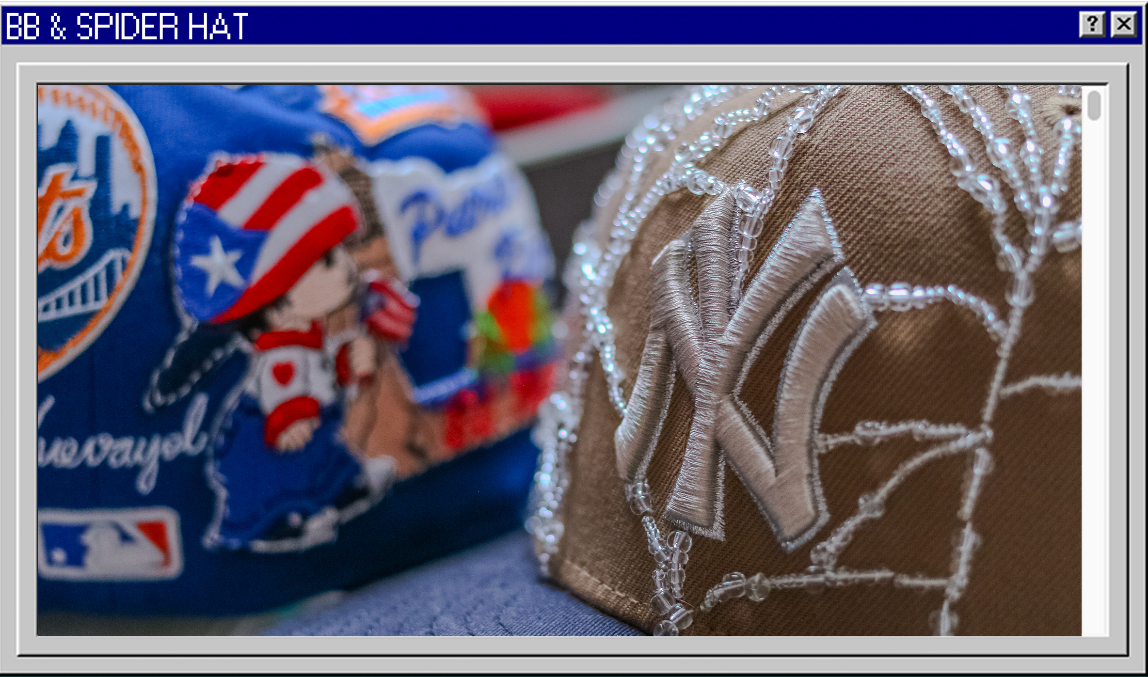Close-up of a brown fabric cap with an embroidered New York Yankees logo and clear bead embellishments, with colorful patches including a character with an American flag-themed hat in the background.