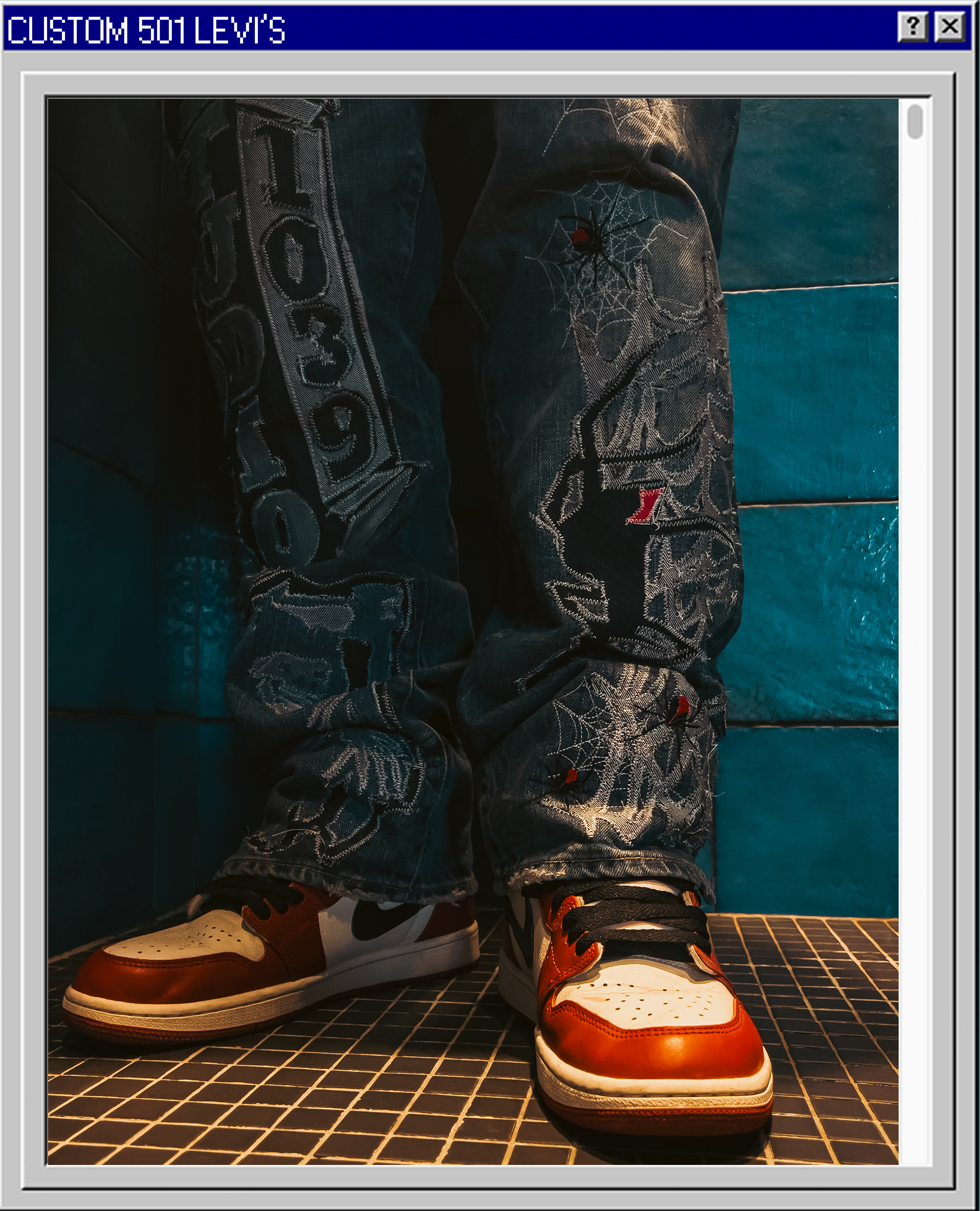 Close-up of a person wearing jeans with embroidered patches and sneakers, standing on a tiled floor against a teal tiled wall background.