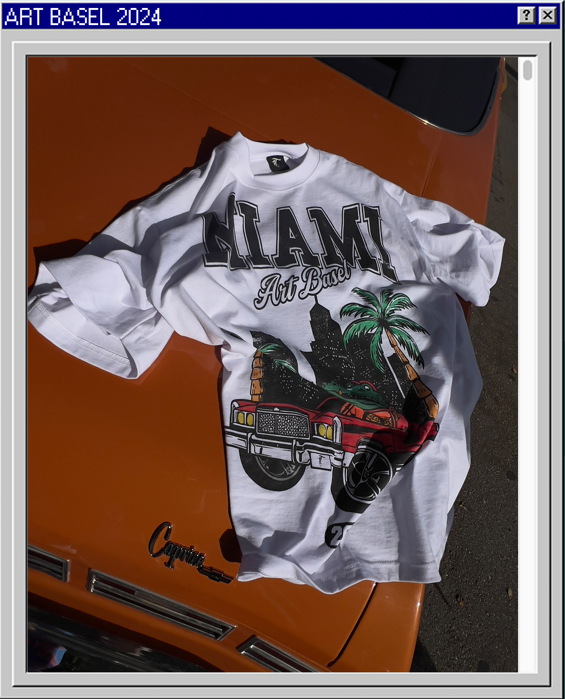 A white T-shirt with a graphic design of a cityscape, palm trees, a red car, and a crocodile, laid on the hood of an orange Pontiac car. The shirt has text reading 'MIAMI' and 'Art Basel'.