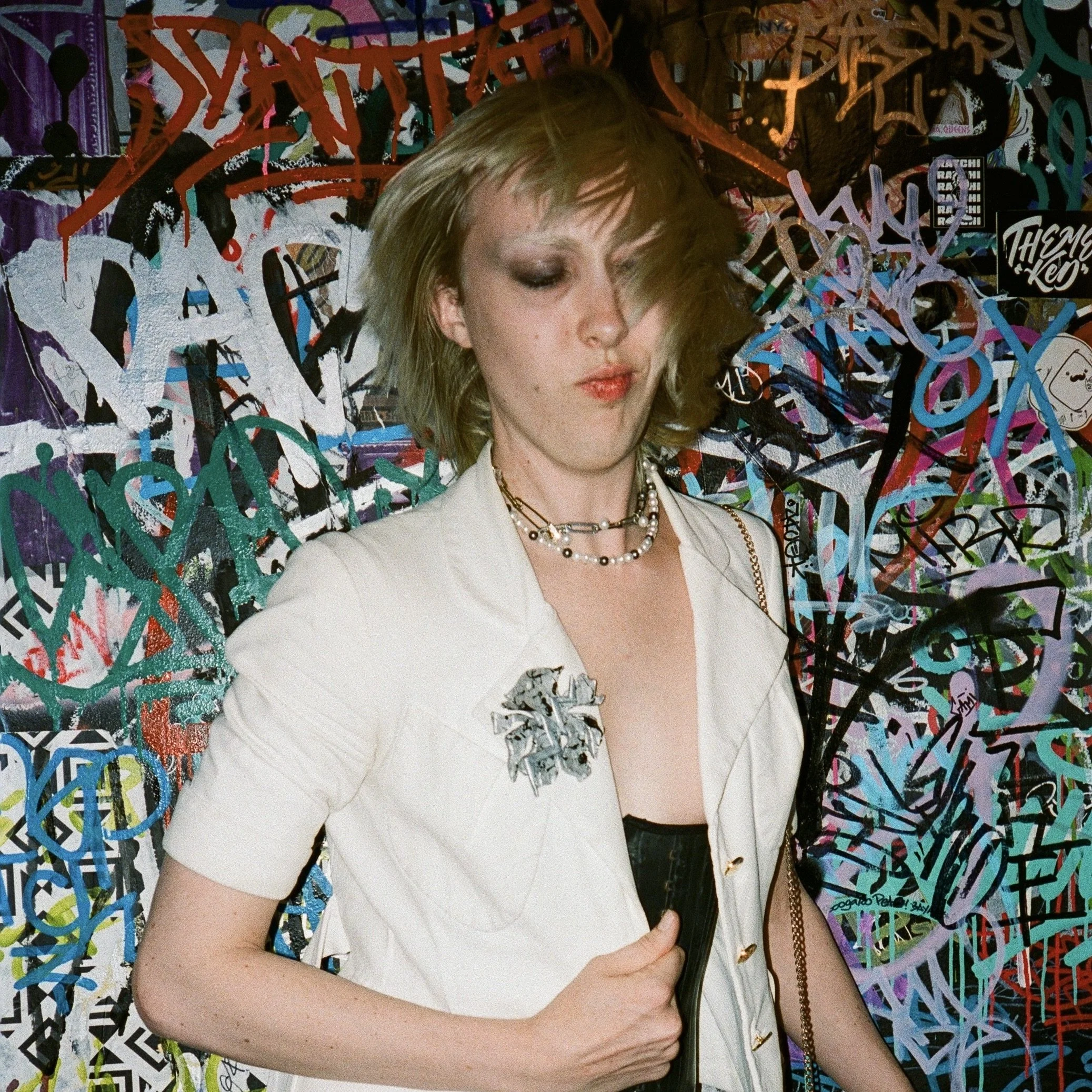 Woman with short blonde hair in a white outfit standing in front of a colorful graffiti wall.