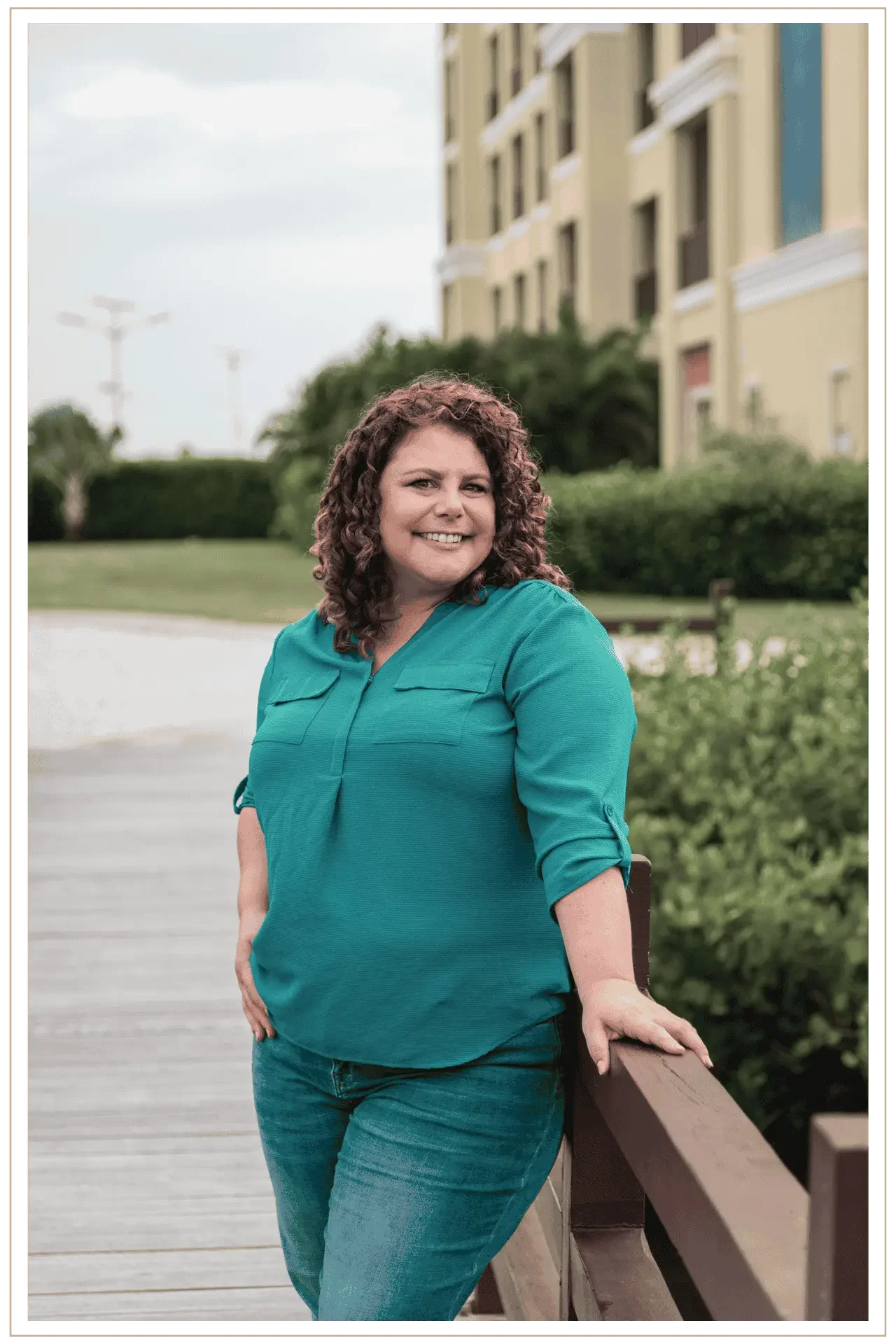 Denise Kubica, luxury travel advisor and founder of Mindset Travel, smiling and leaning against a wooden railing in an outdoor European-style setting with a multi-story building and greenery in the background.