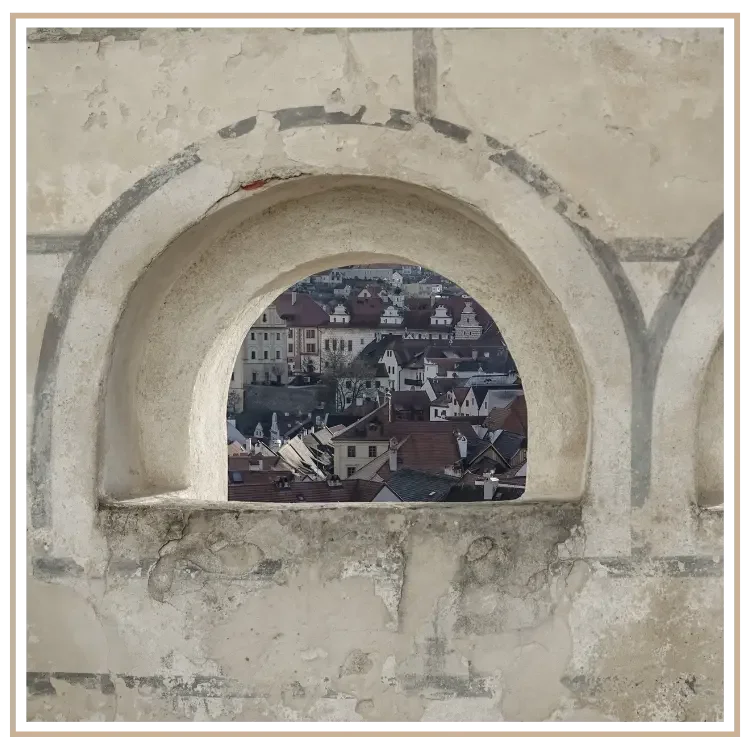 The Old Town of Cesky Krumlov seen through an arched opening in a wall.