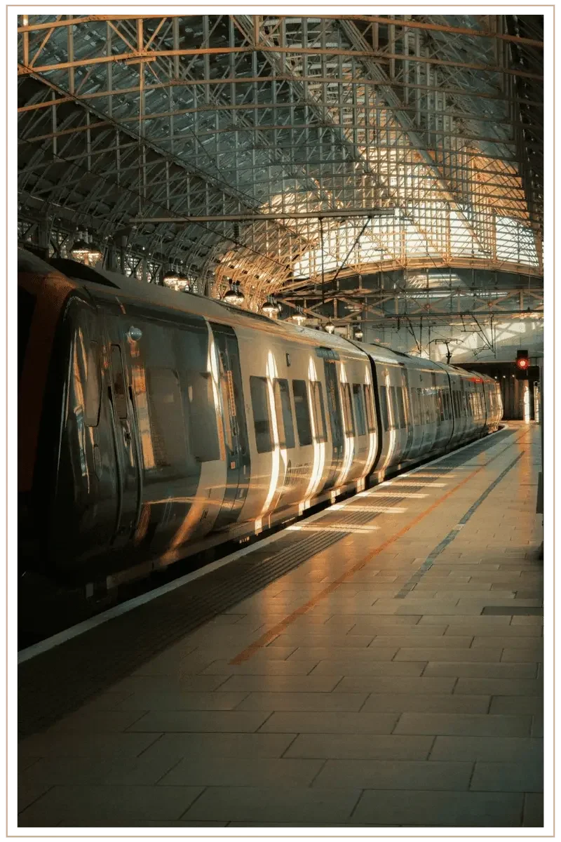 A modern high-speed passenger train waits at a tiled platform under the complex, vaulted steel and glass lattice structure of a railway station at dawn.
